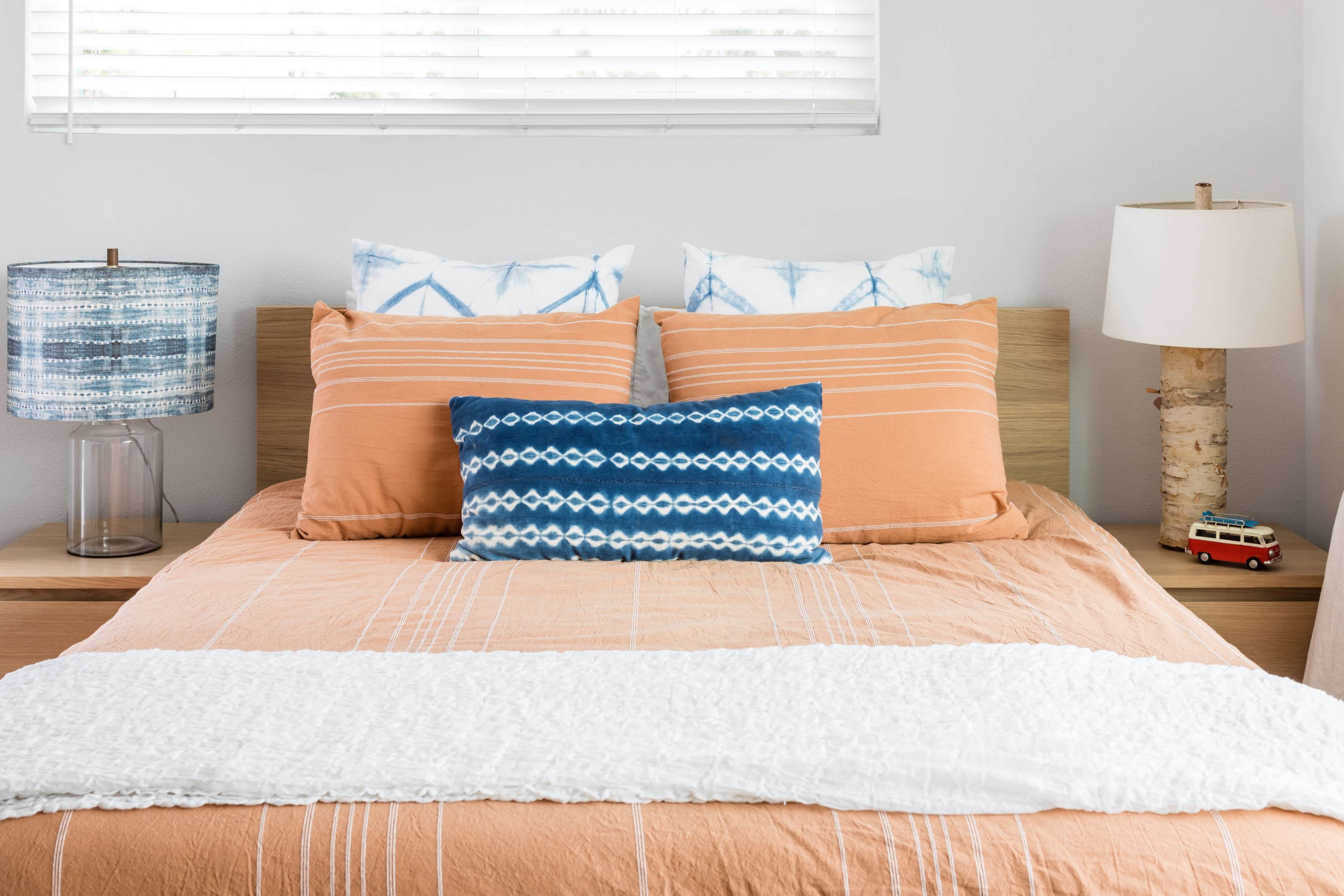 A neatly arranged bedroom features an orange bedspread with multiple textured pillows, a wood headboard, and bedside lamps.
