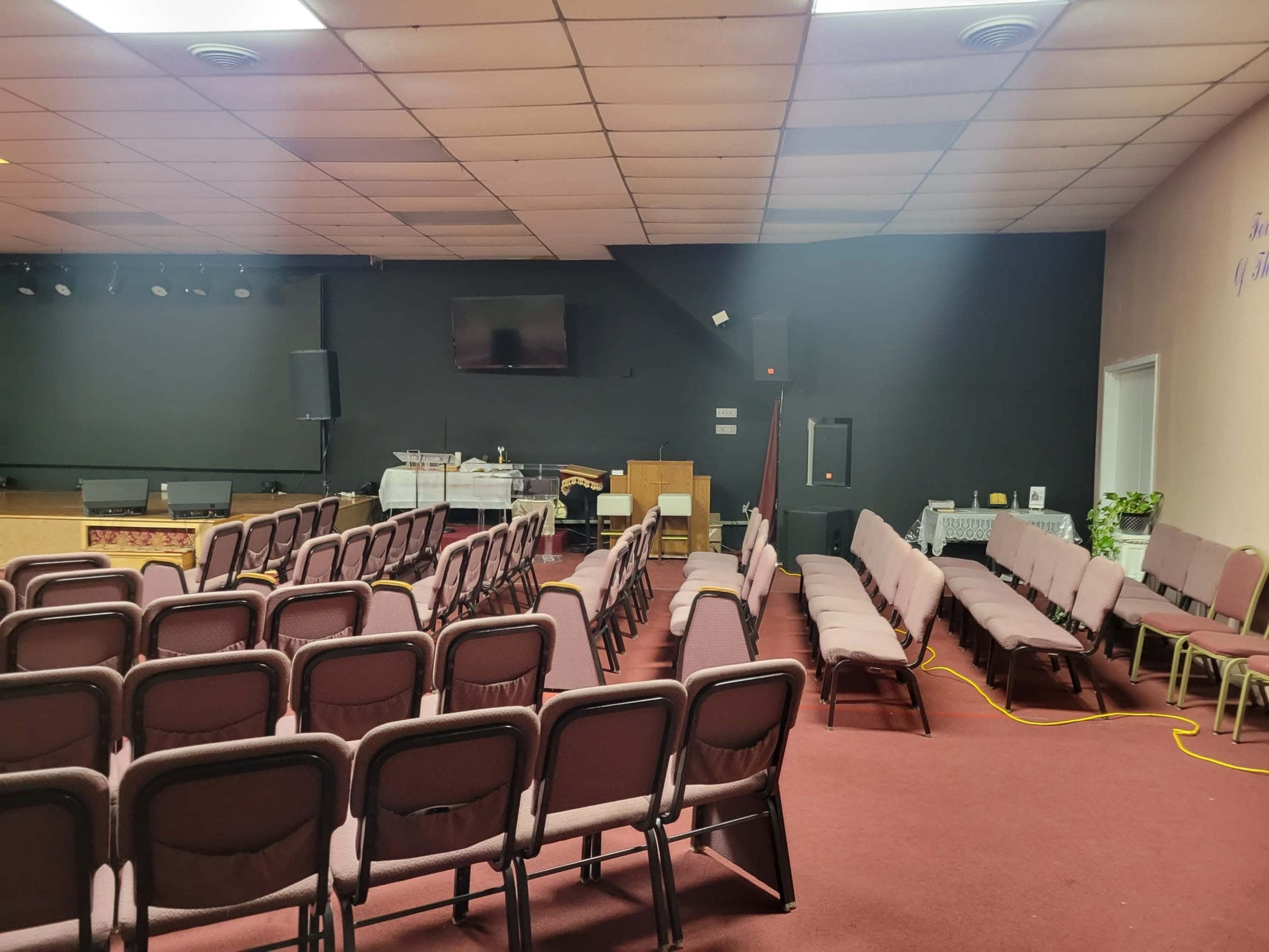 A room set up for an event, with rows of chairs facing a stage and a wall-mounted screen.