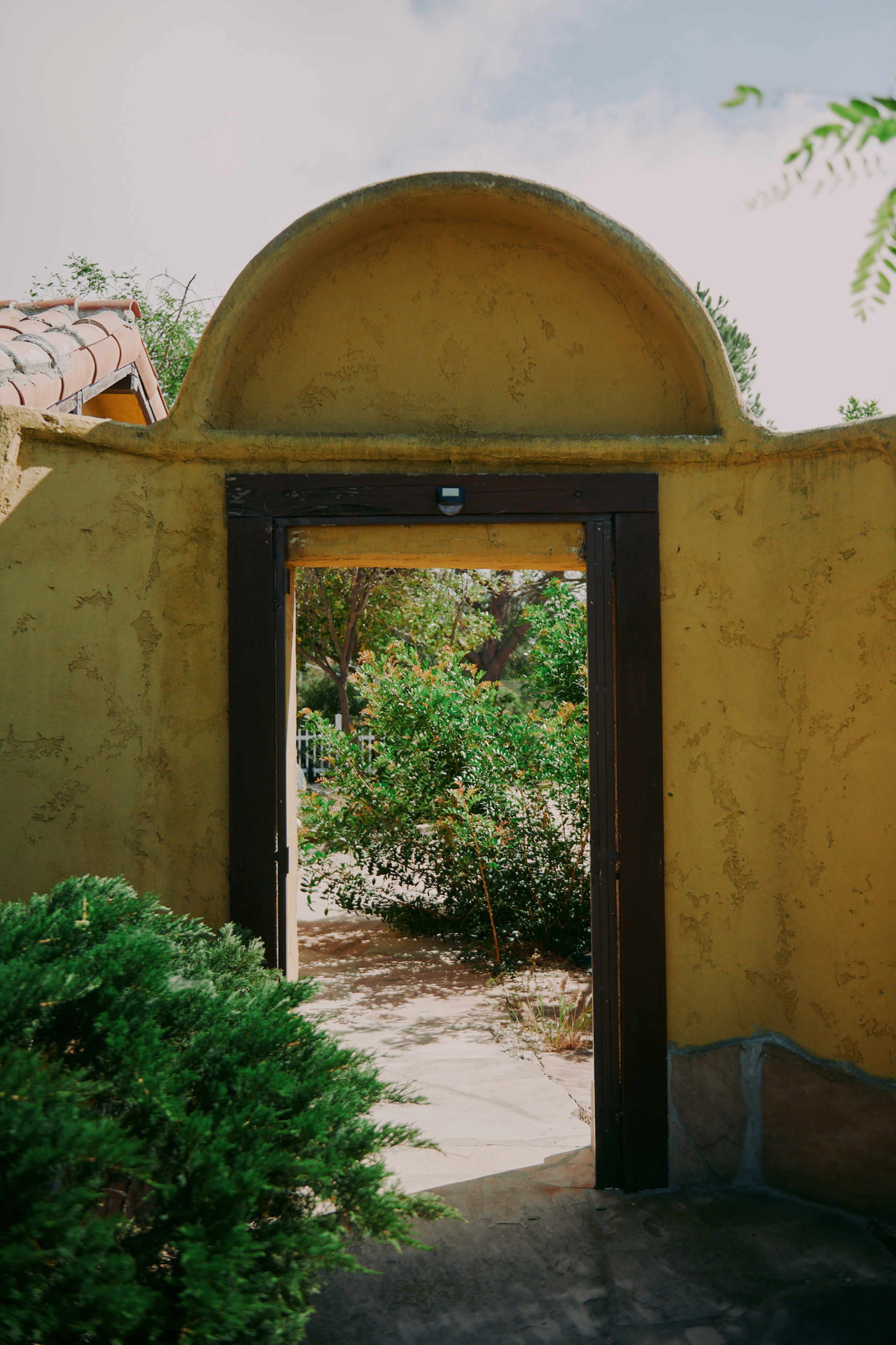 An archway leads to a garden with green foliage and a clear sky.