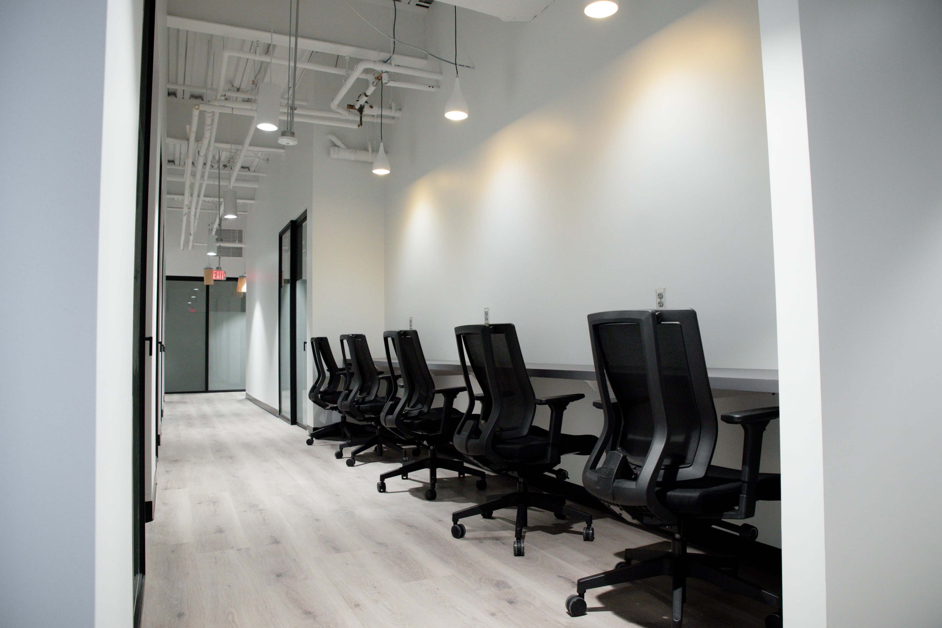 The image shows a hallway with a row of office chairs lined against a light-colored wall in a modern workspace.