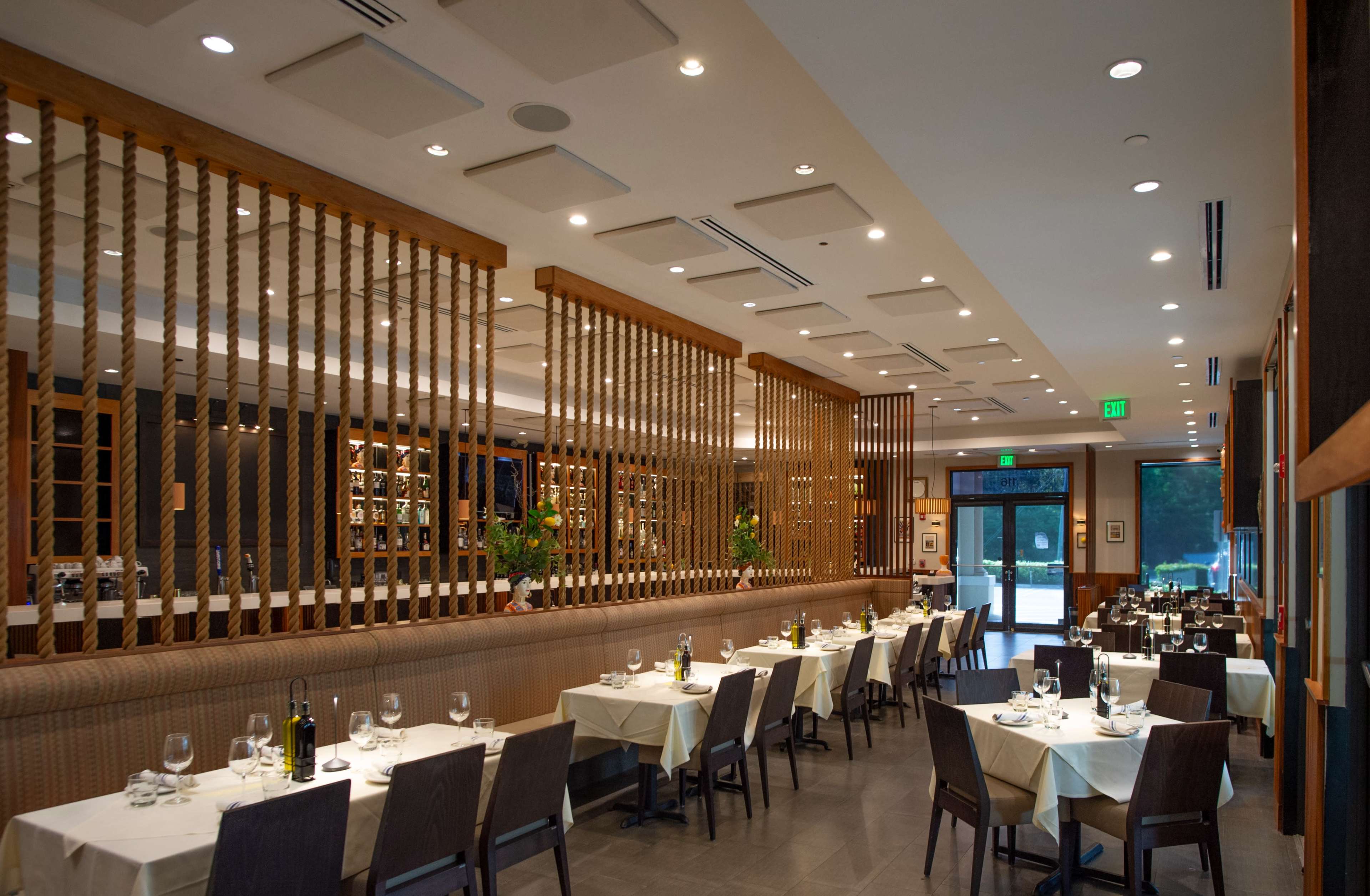The image shows a modern restaurant interior with neatly arranged tables and a wooden partition separating the dining area from the entrance.