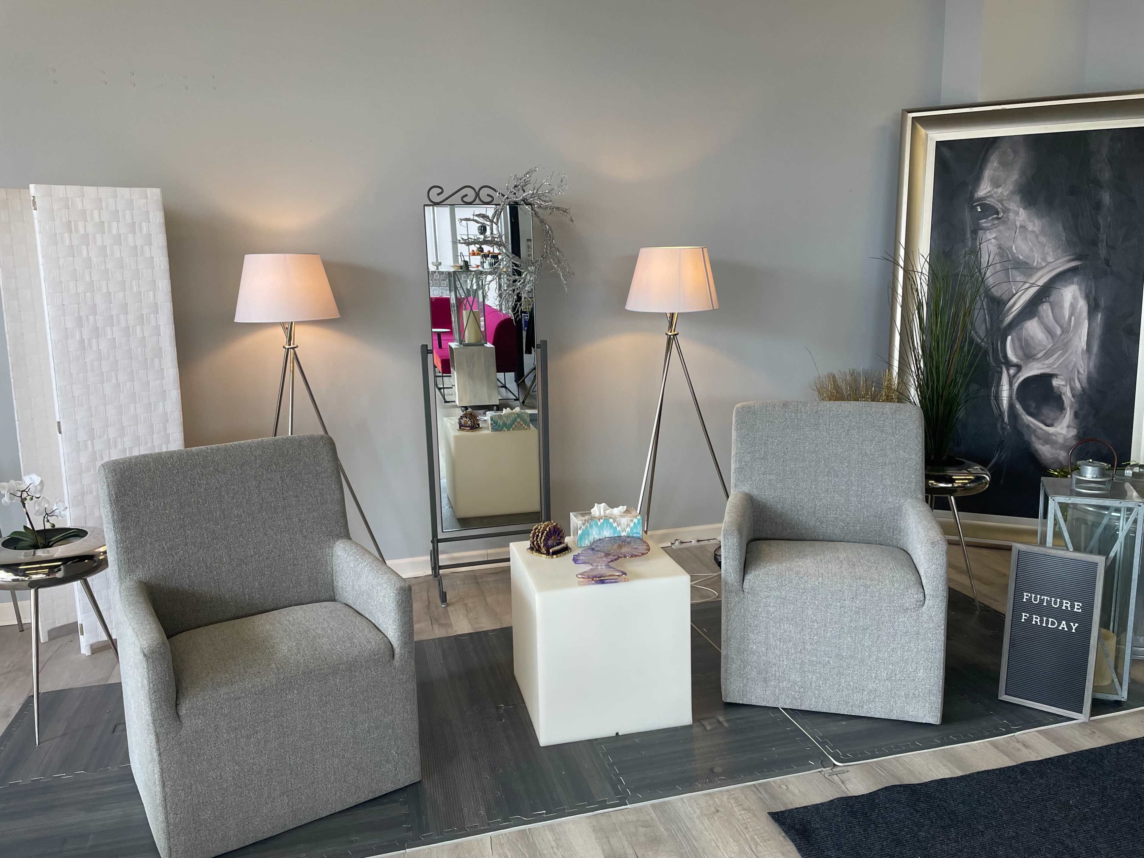 Two gray armchairs positioned near a mirror and lamps, with a small table and decorative items in a softly lit room.