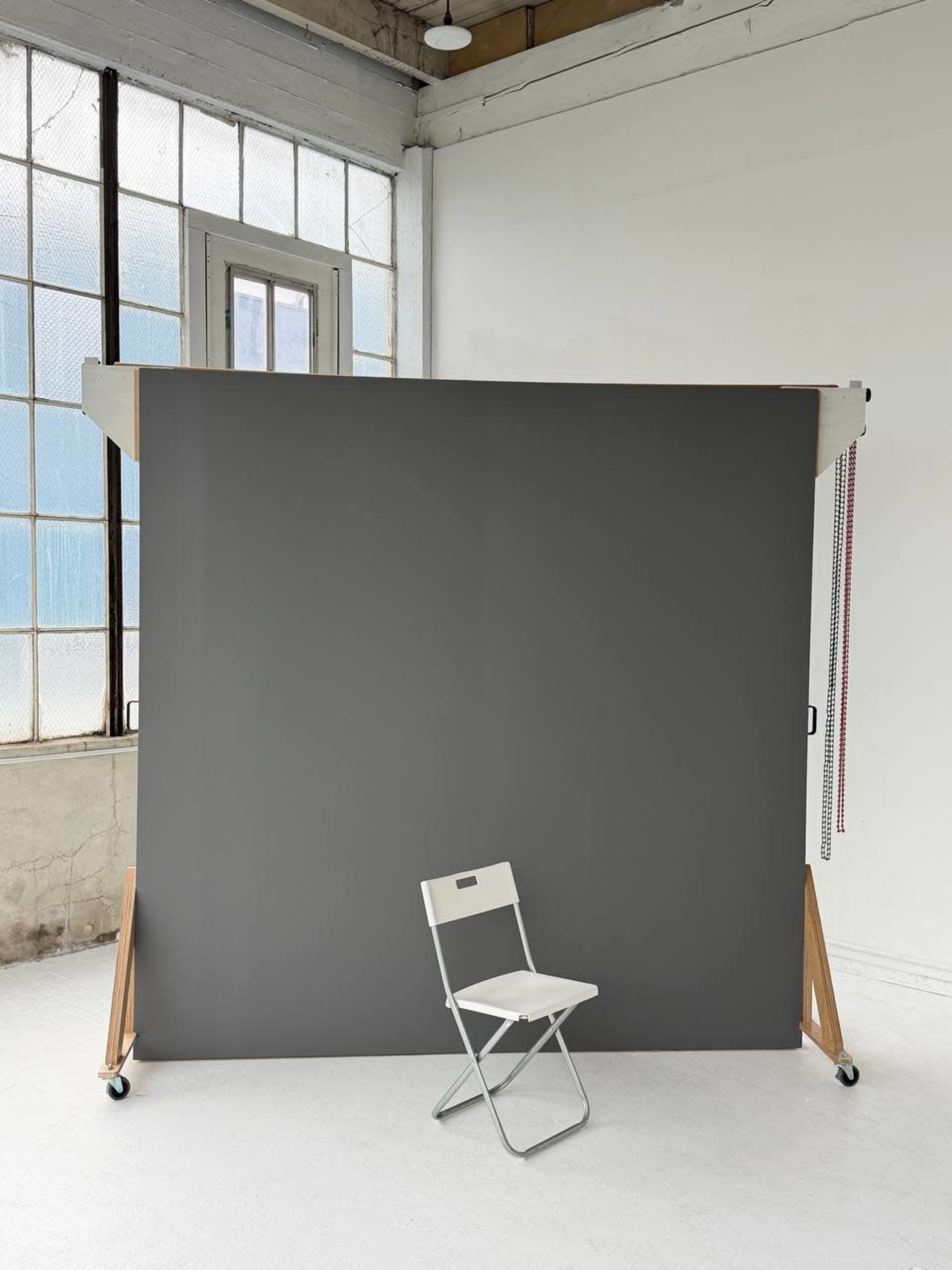 A gray backdrop stands in a well-lit room with a single white folding chair in front of it.