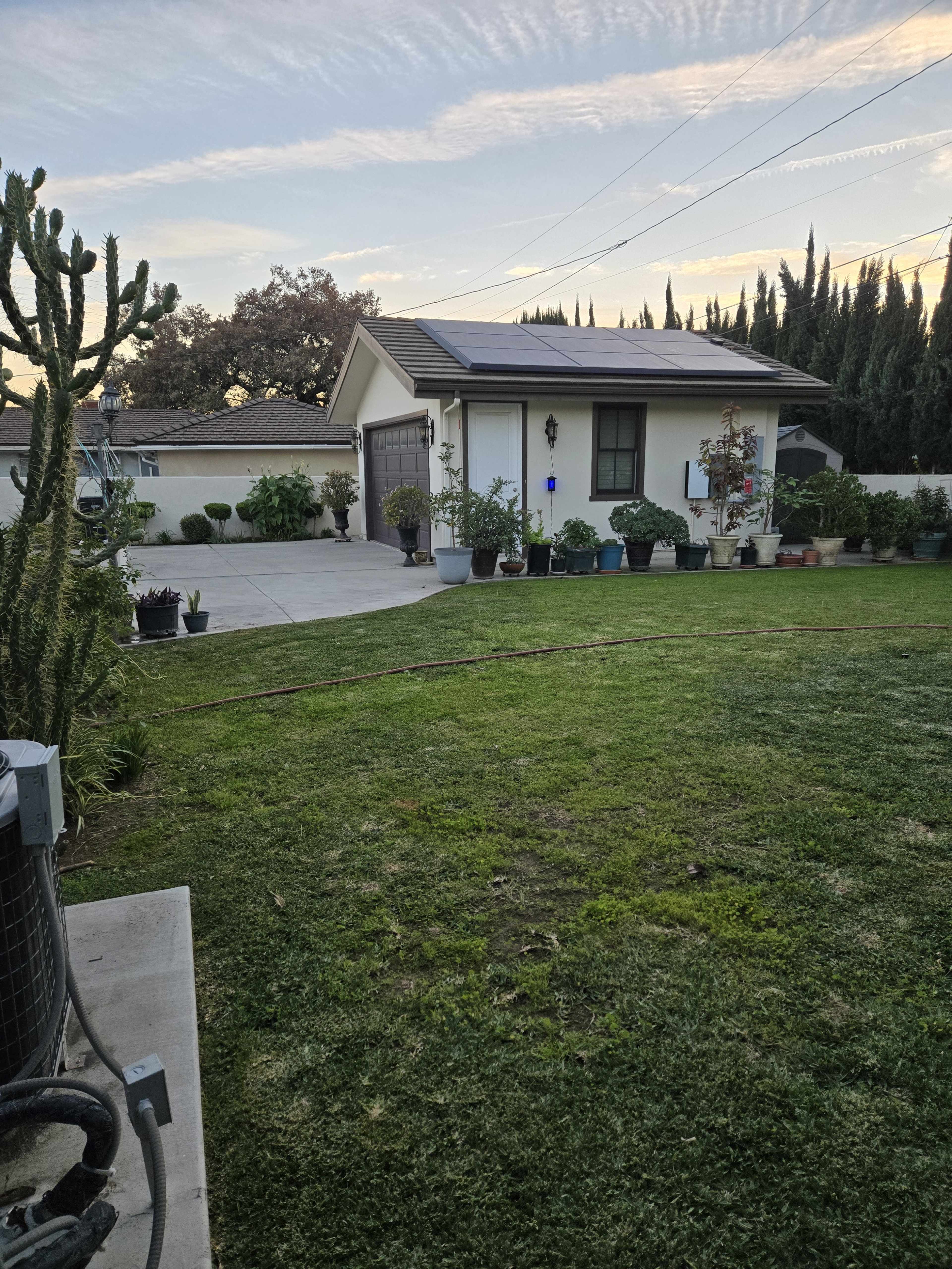 A well-maintained backyard features a neatly trimmed lawn, potted plants, and a house with solar panels on the roof.