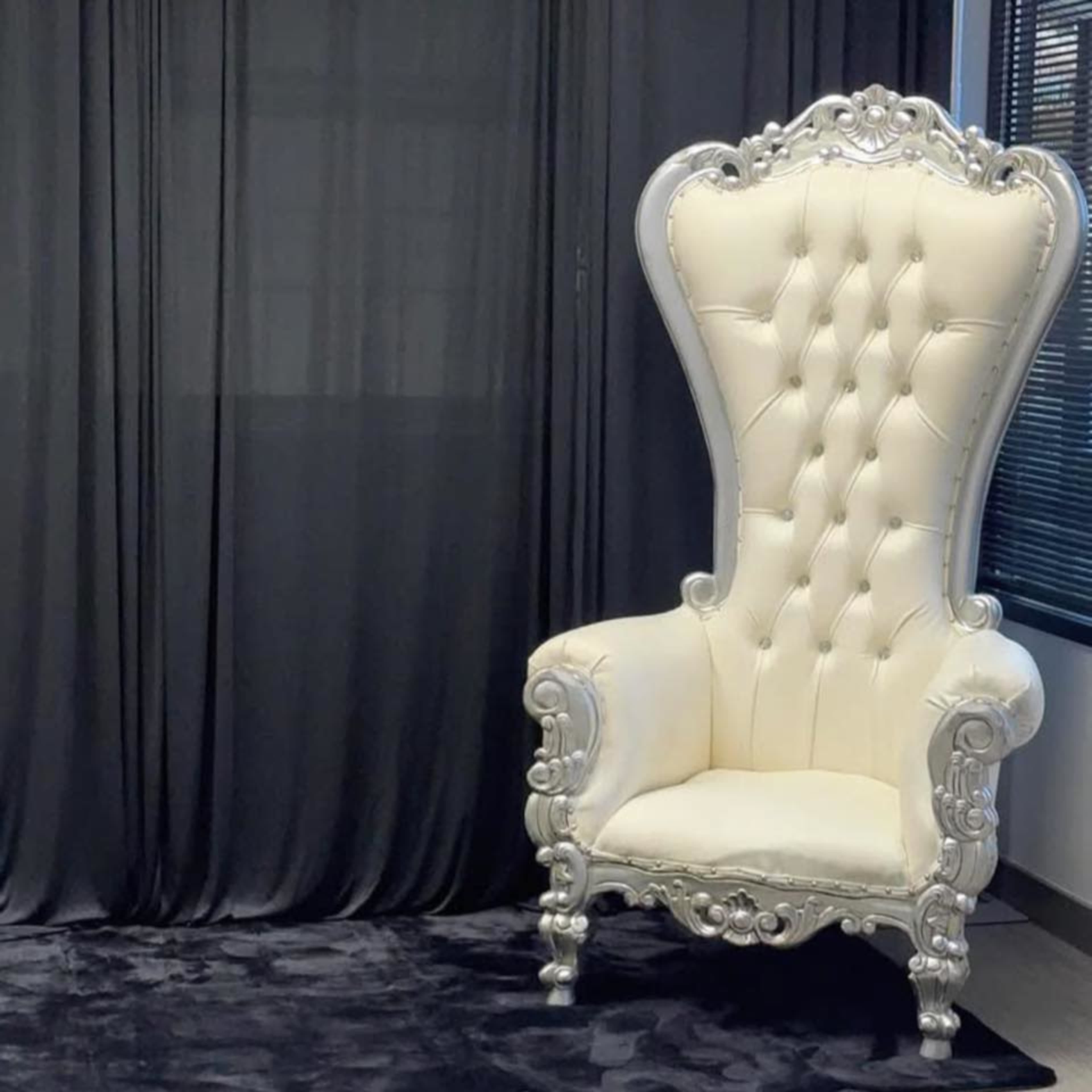The image shows a large, ornate white throne with a tall backrest and silver accents, set against a black backdrop in a room.