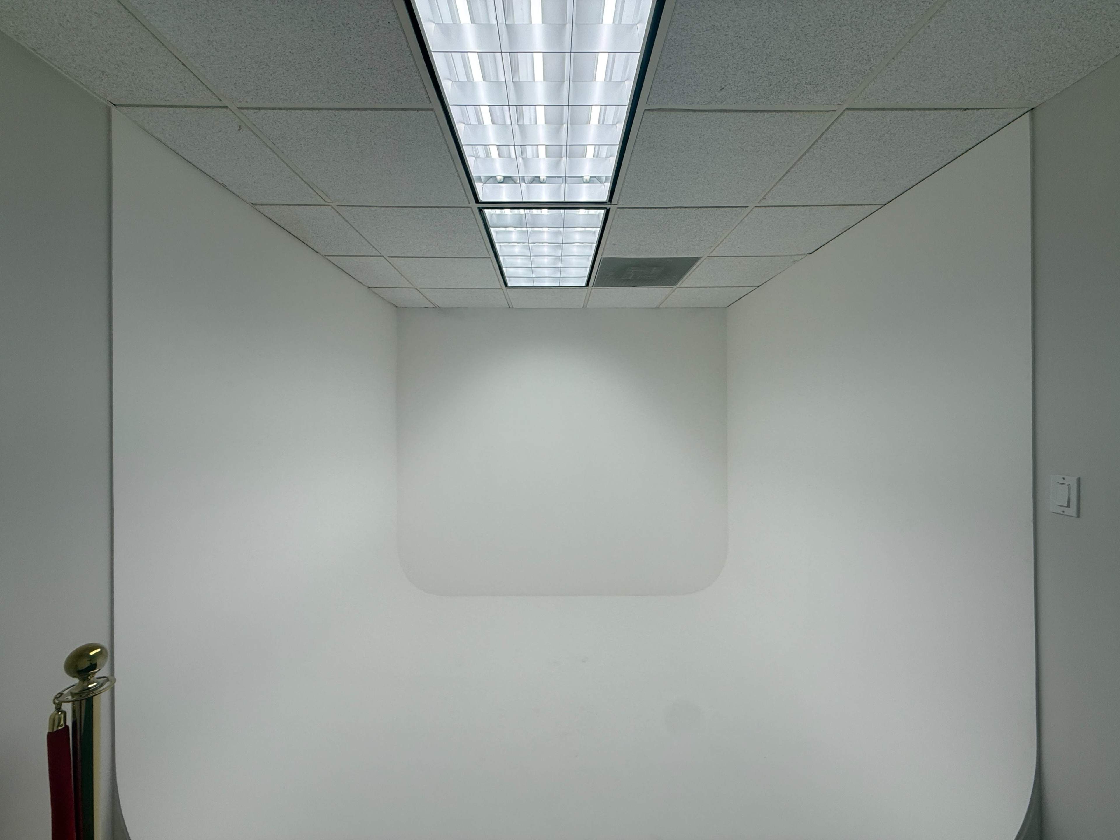 A stark, empty room features a ceiling light and plain white walls with no furniture or decorations.
