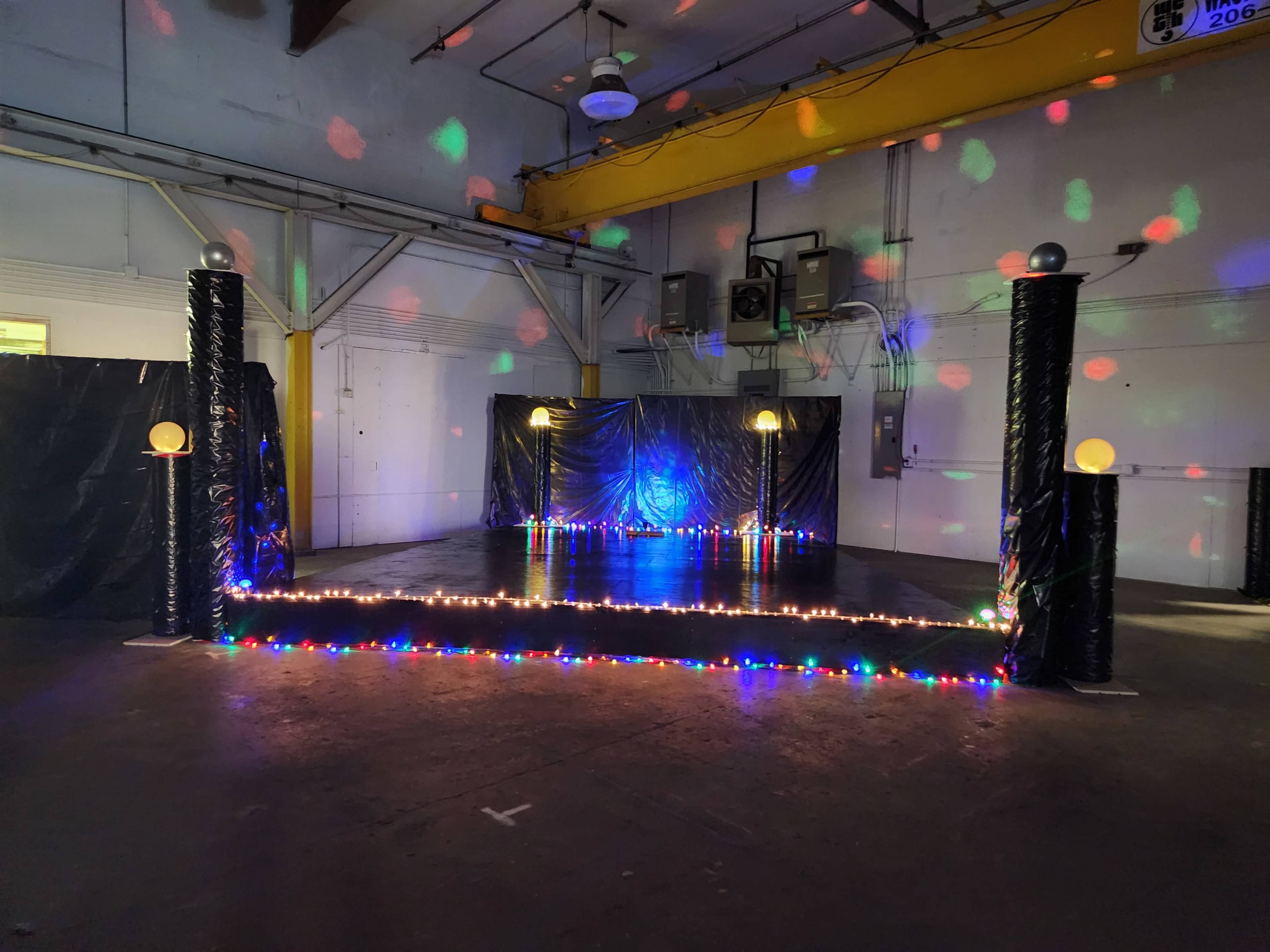 The image shows an empty dance floor area decorated with colorful lights and illuminated columns in a large, industrial space.
