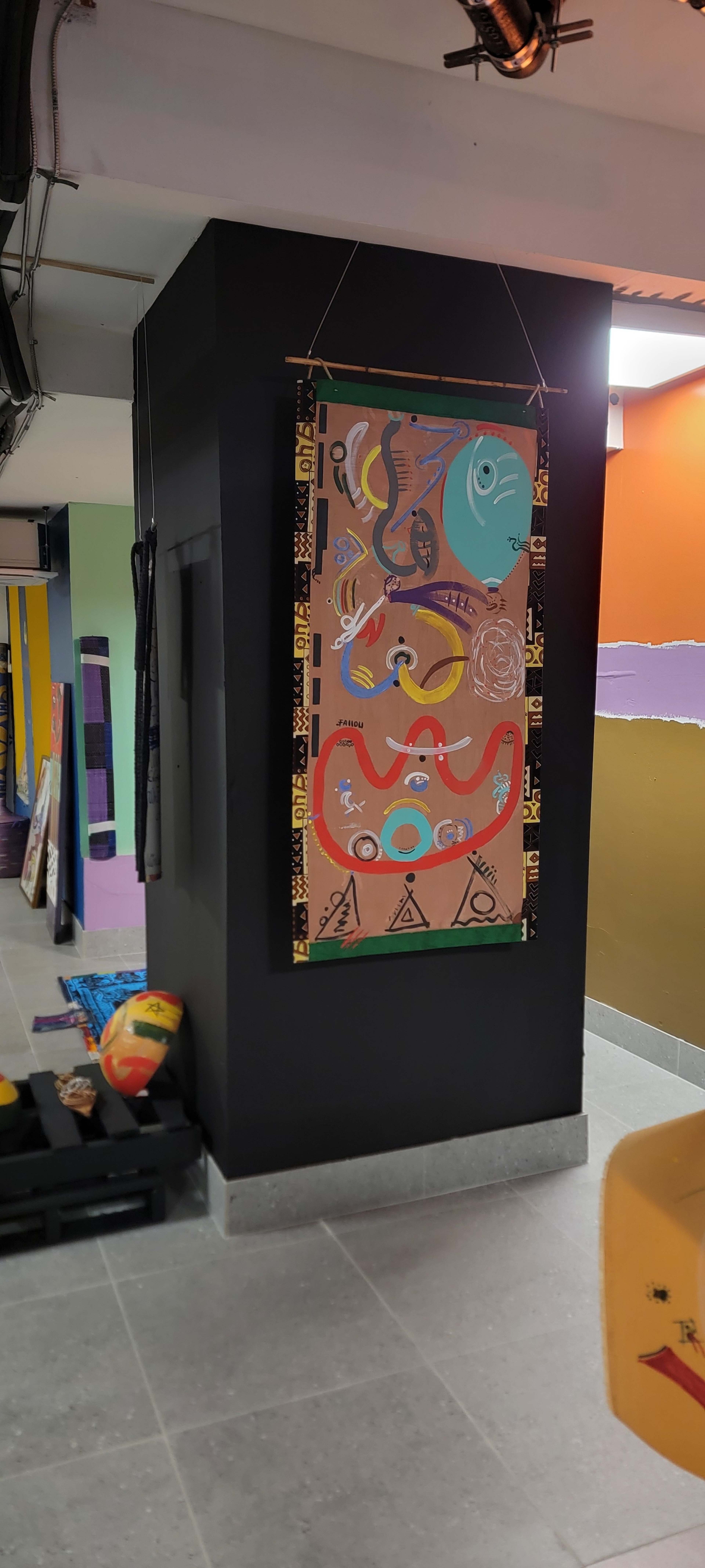 The image shows a colorful wall mural hanging in a hallway that features abstract shapes and symbols, with varied colors and designs.