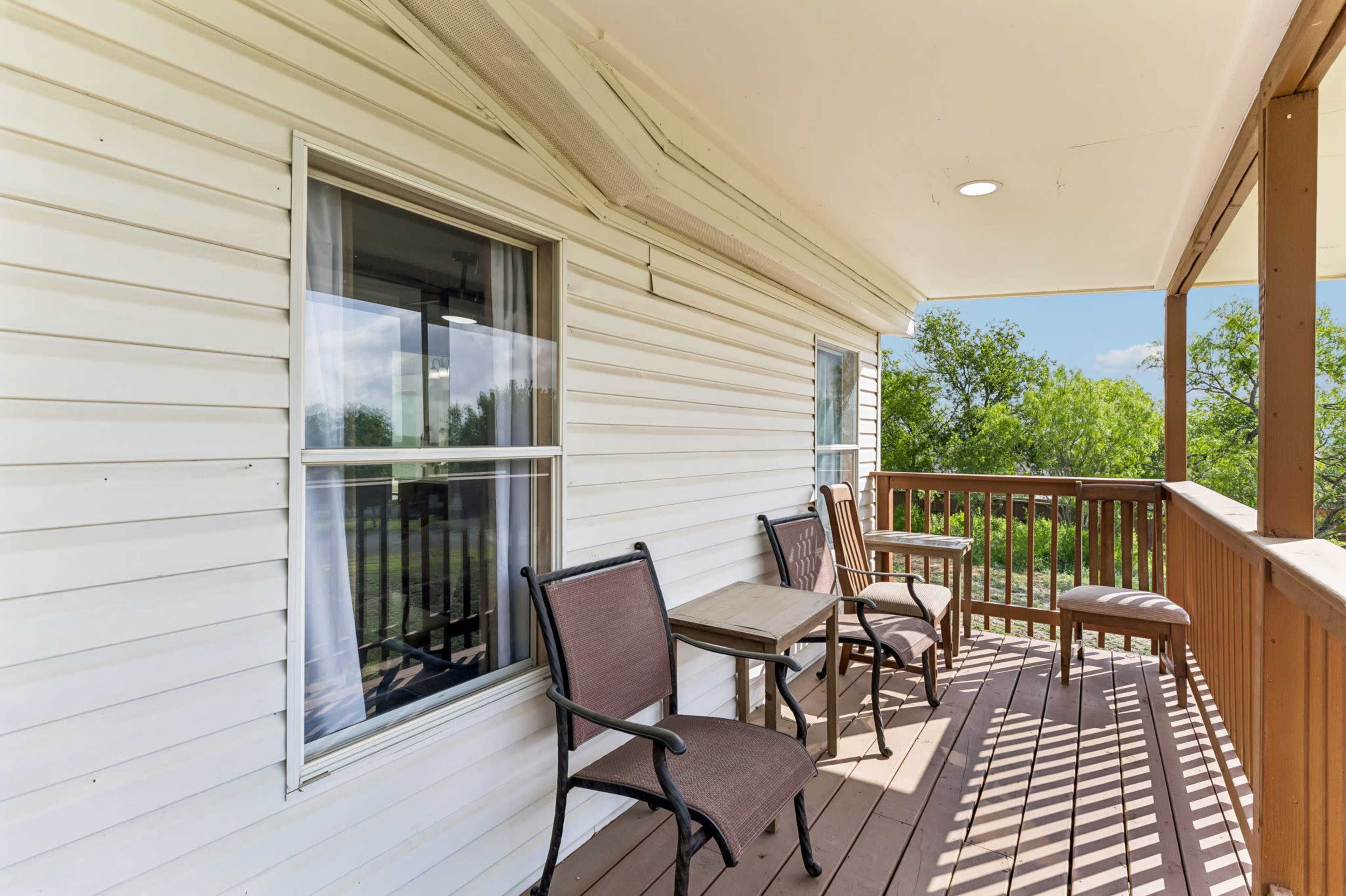 The image shows a covered porch with two chairs and a small table, overlooking a green area.