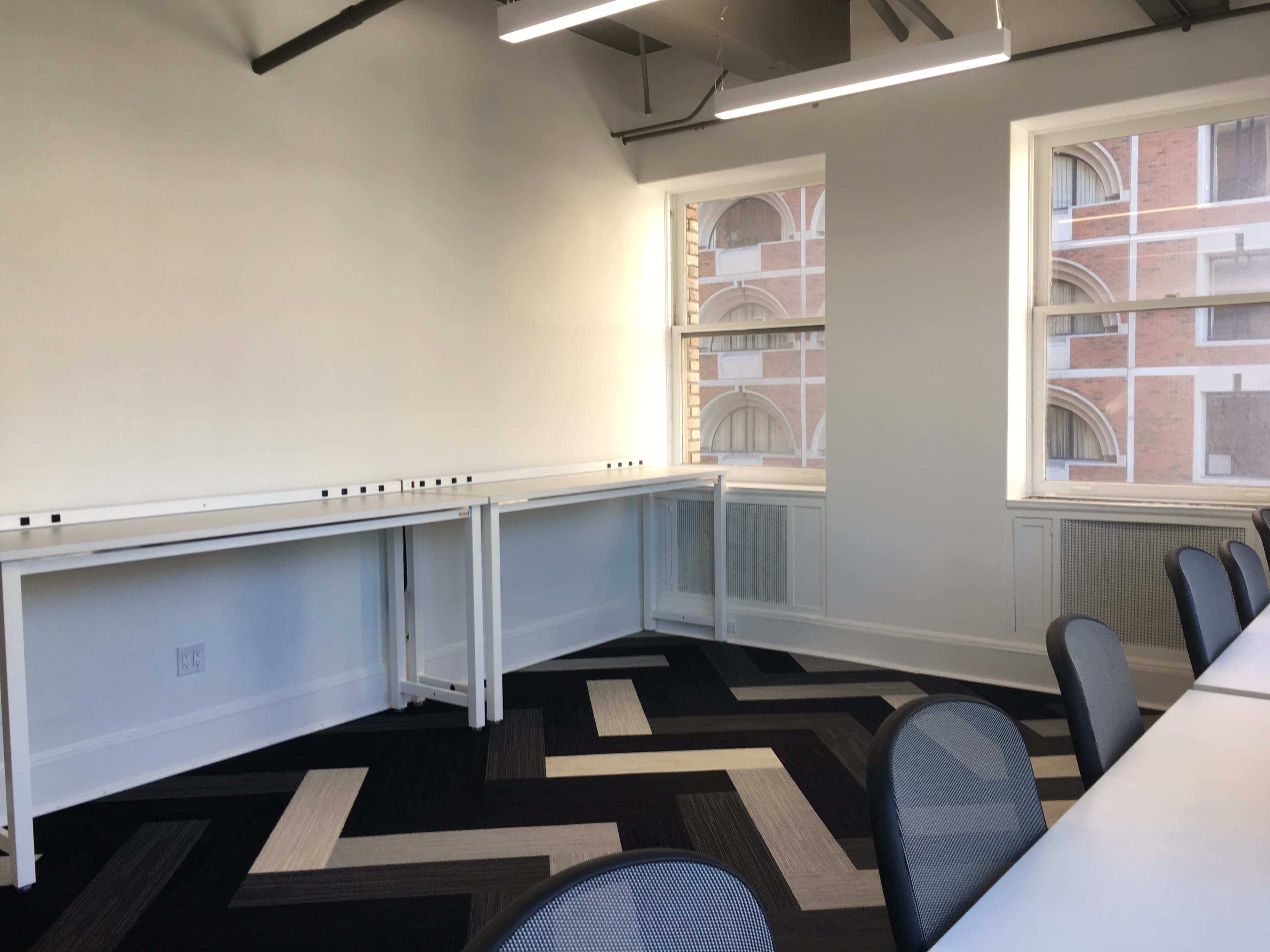 A bright meeting room with two white desks along the walls and a zigzag patterned black and white carpet.