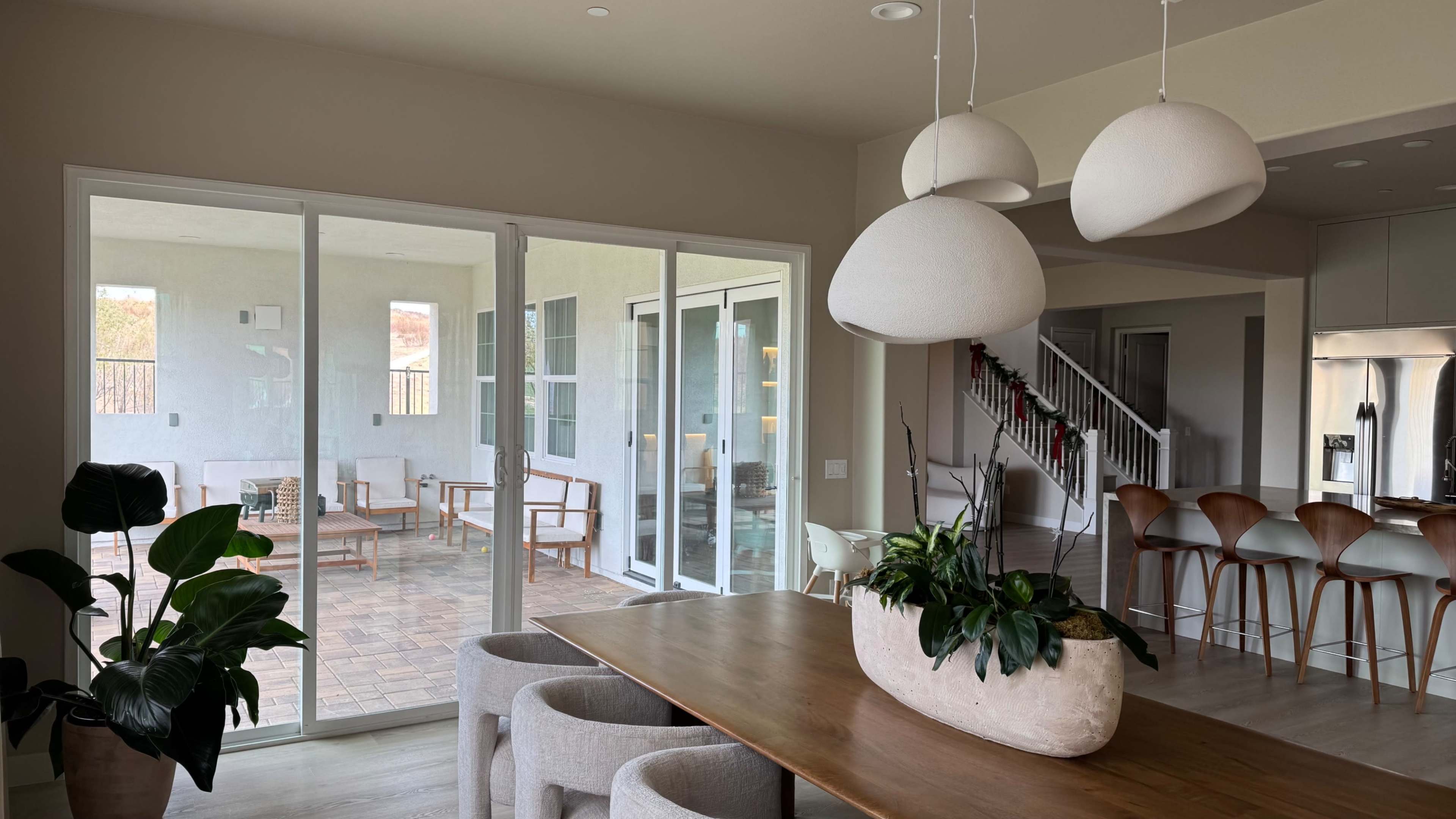 The image shows a modern dining area with a large wooden table and curved chairs, overlooking a covered patio with several outdoor seating arrangements.
