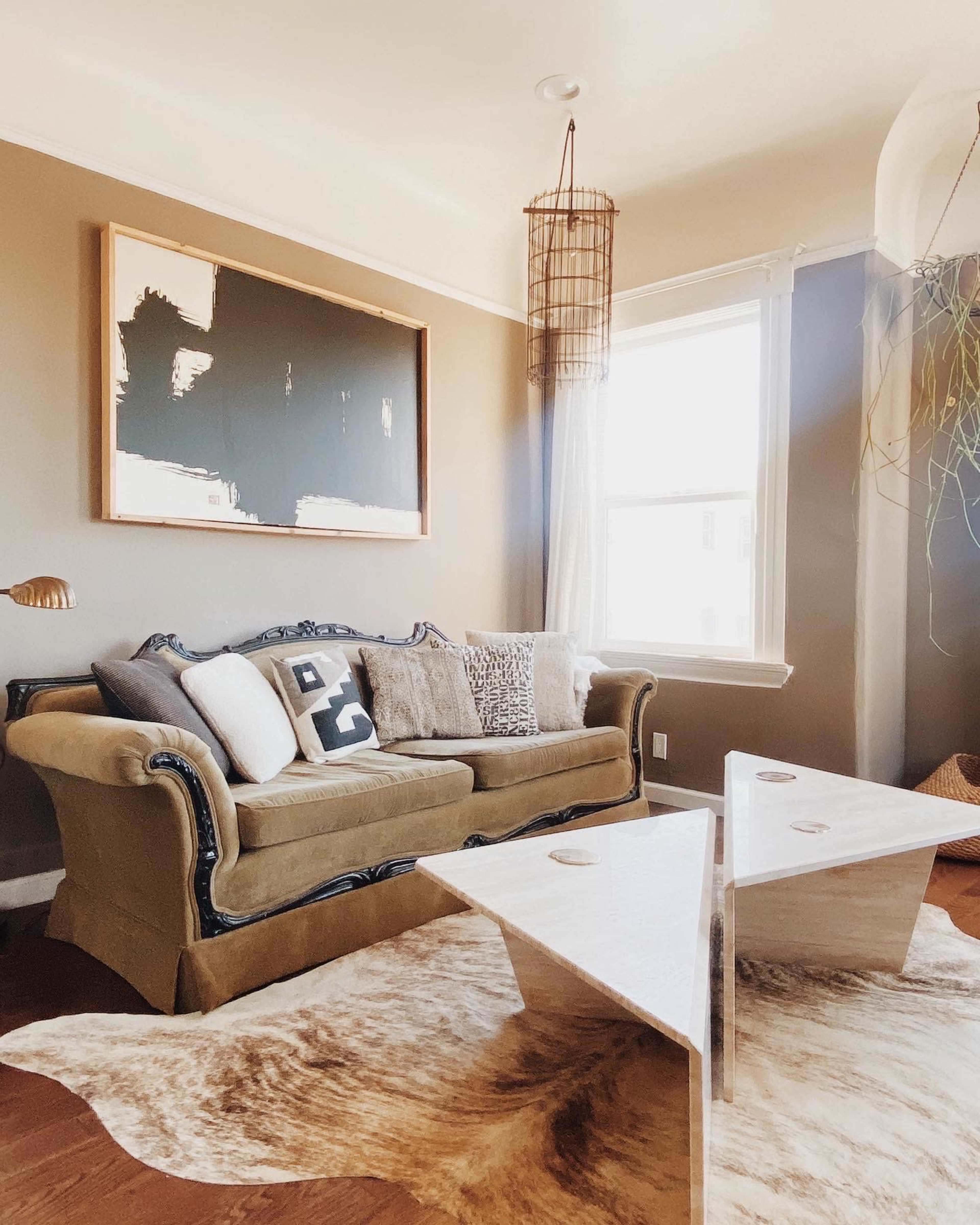 A living room features a green couch with decorative pillows, two triangular tables, and a large wall painting above the couch.