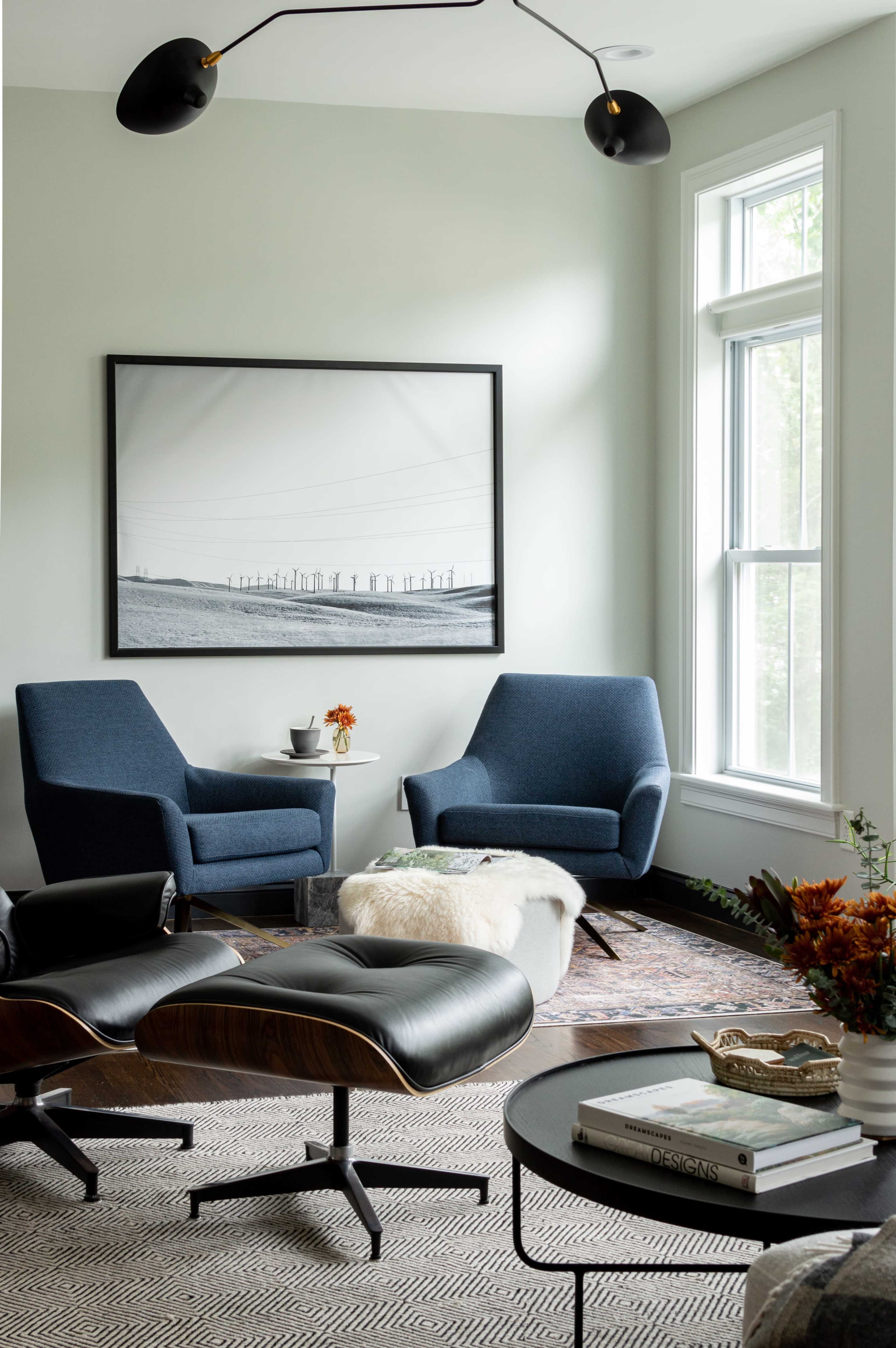 A stylish living room with two blue armchairs, a round coffee table, and a large black-and-white photograph on the wall.