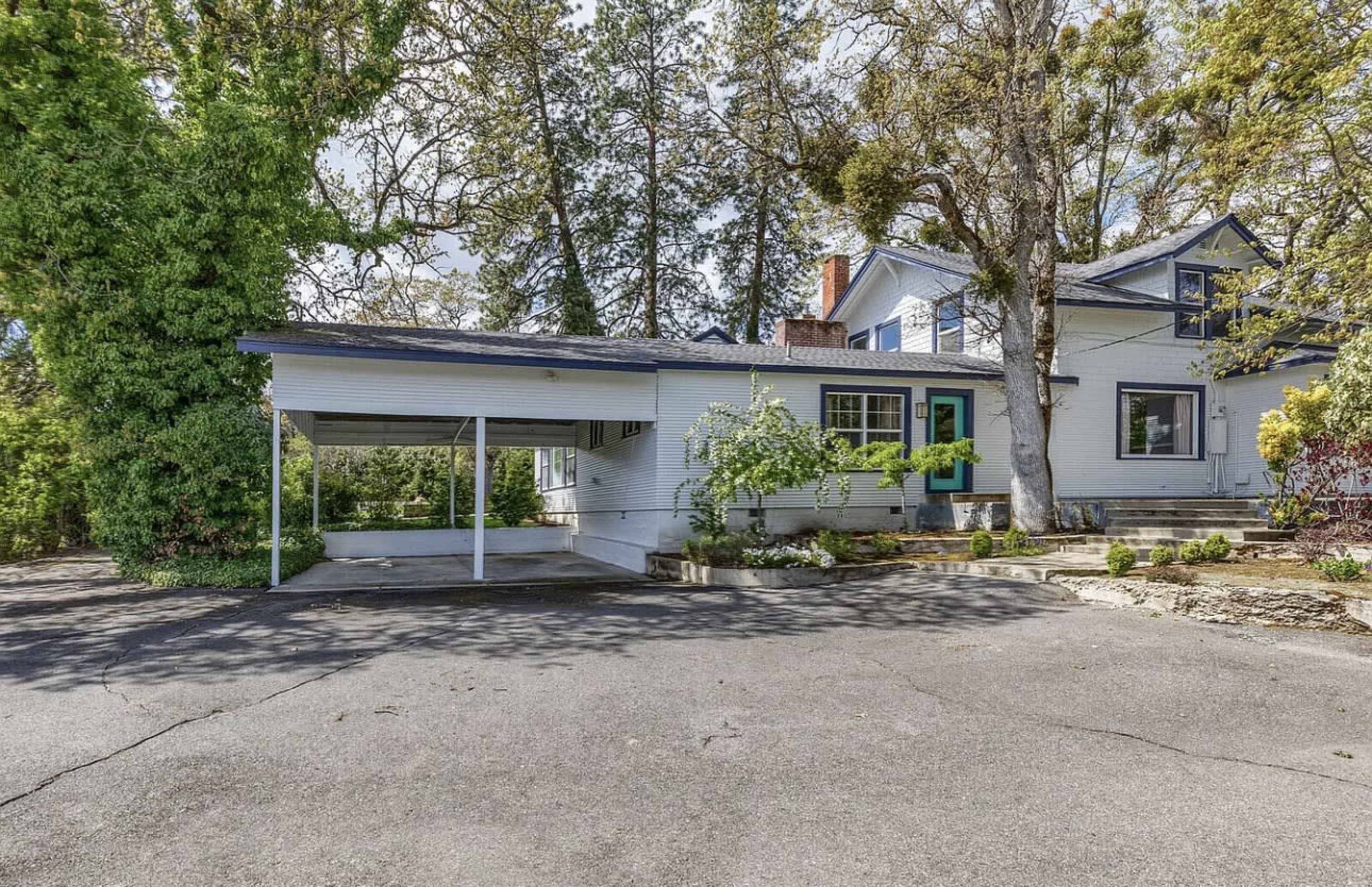 A two-story house with a carport is surrounded by trees and landscaped greenery.