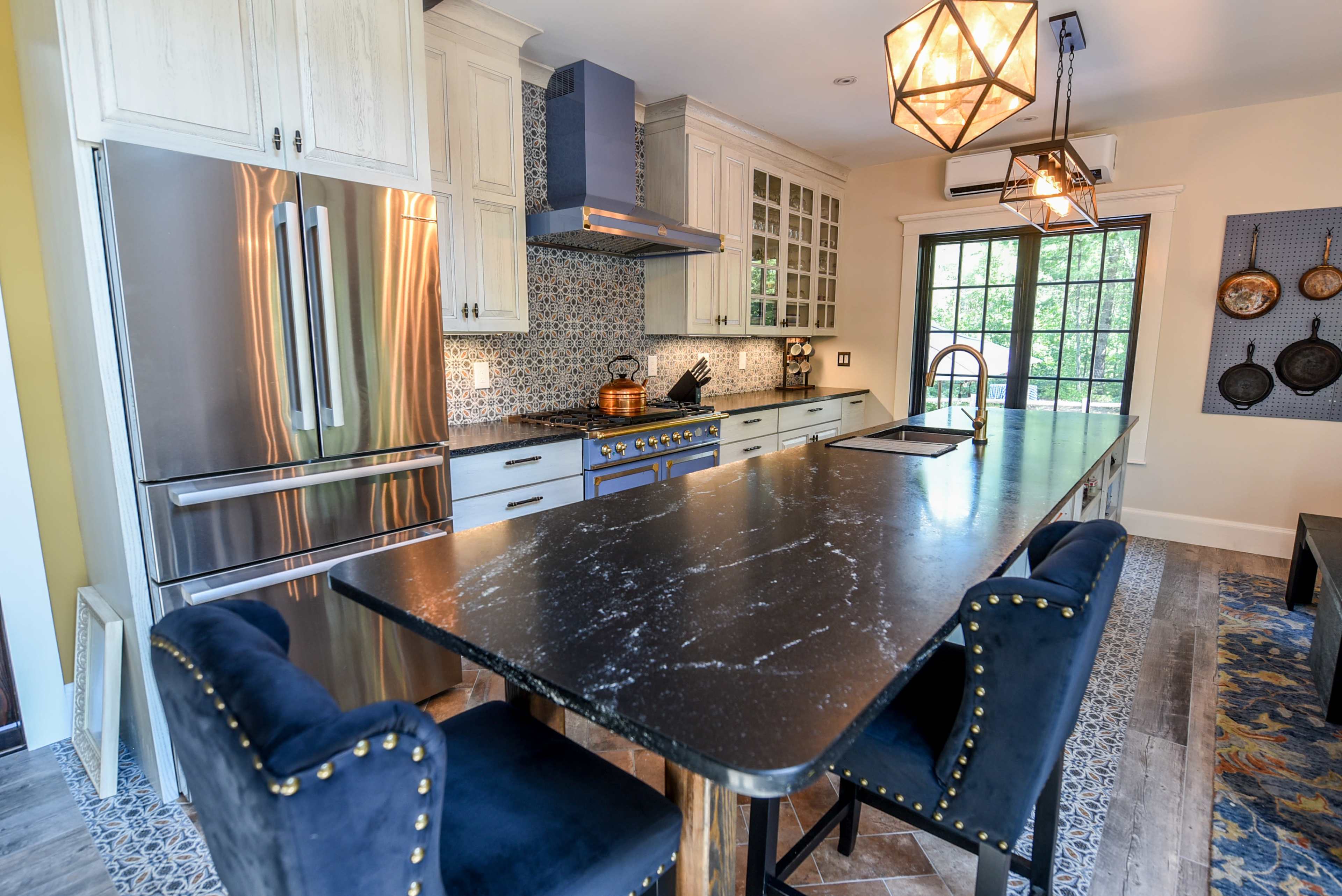 A modern kitchen features a large island with dark countertops, stainless steel appliances, and cabinetry with white and blue accents.