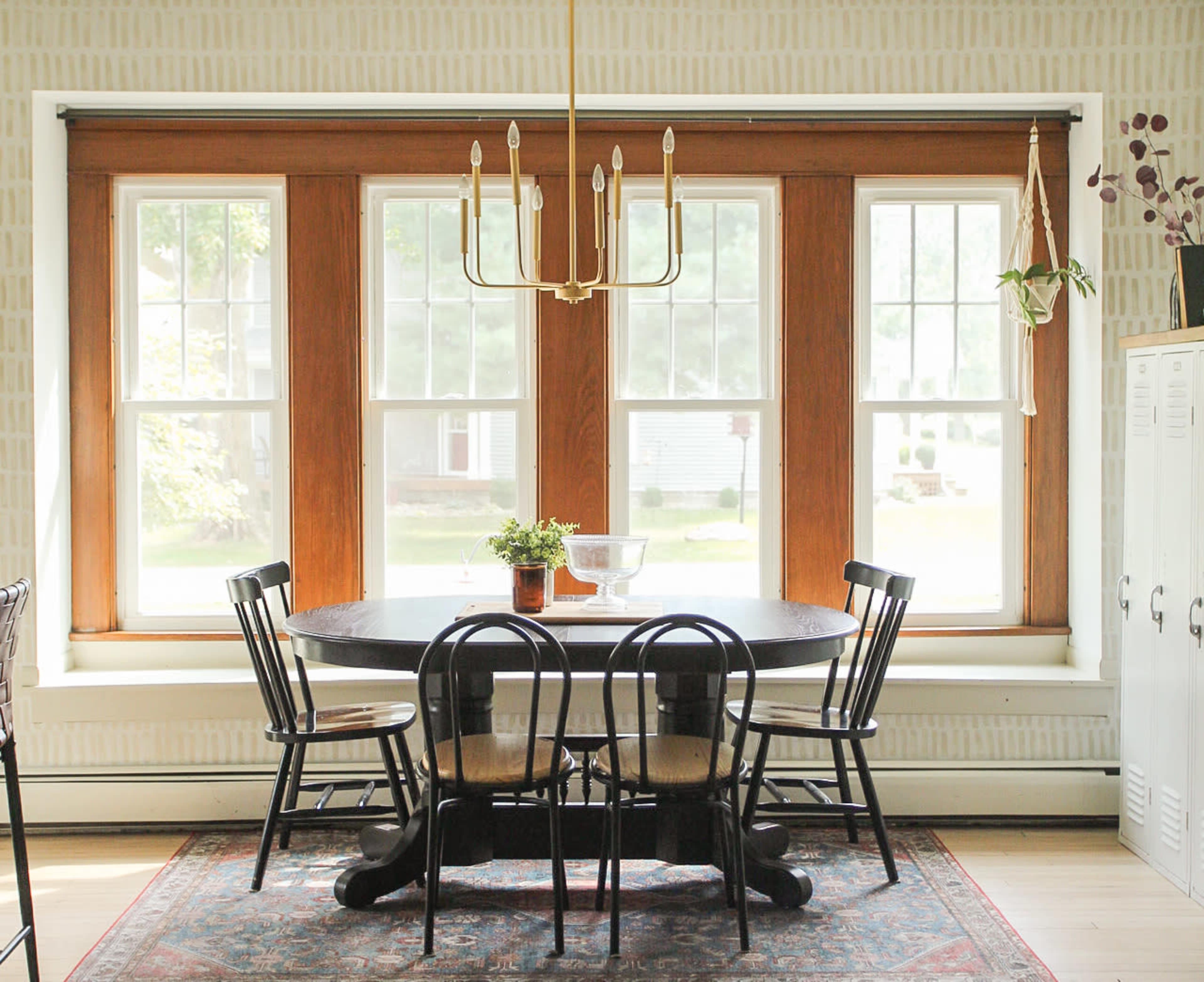 A round black table with four chairs is positioned near large windows with wooden frames in a well-lit dining area.