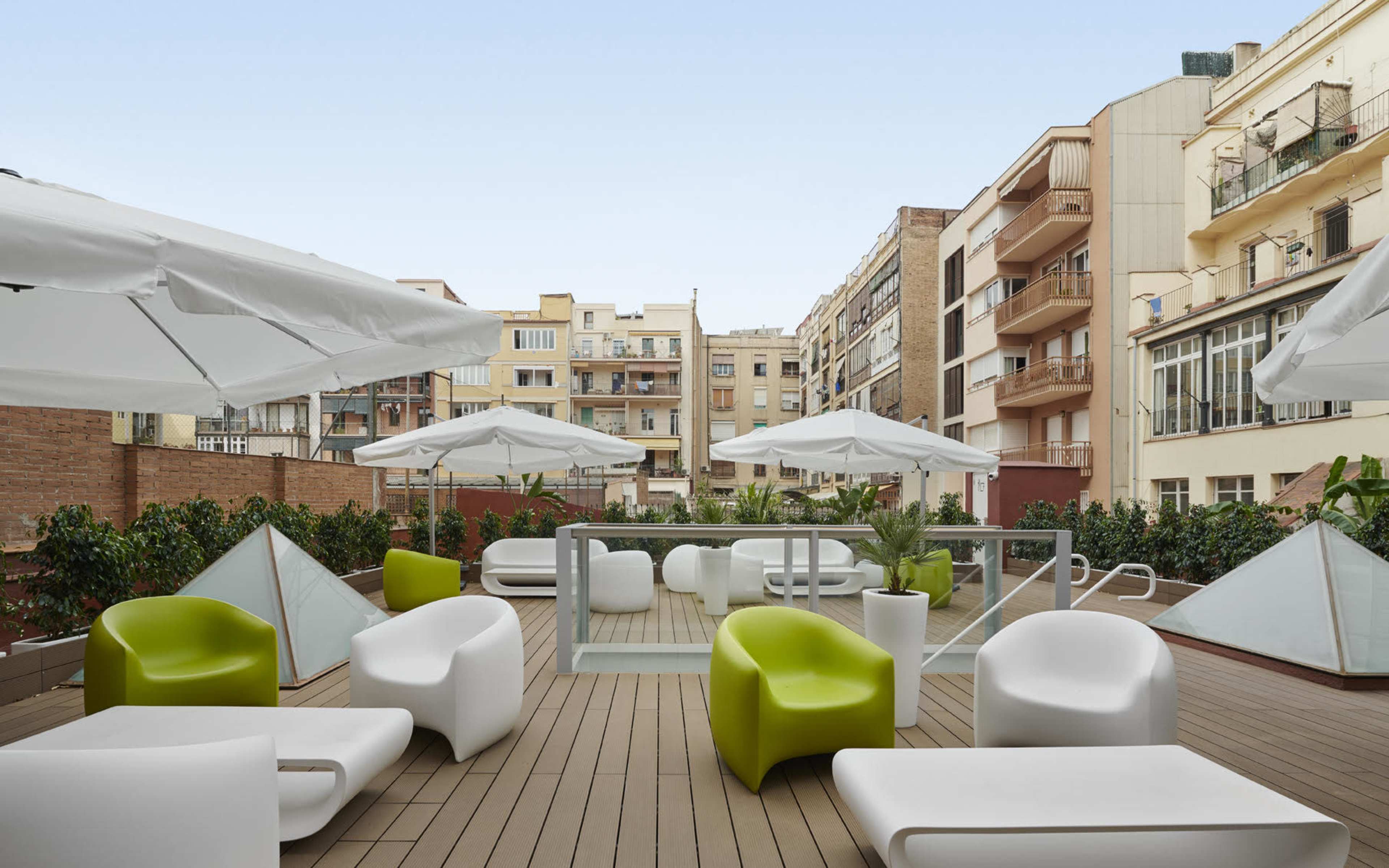 A modern terrace with white and green furniture, umbrellas, and a backdrop of urban buildings.