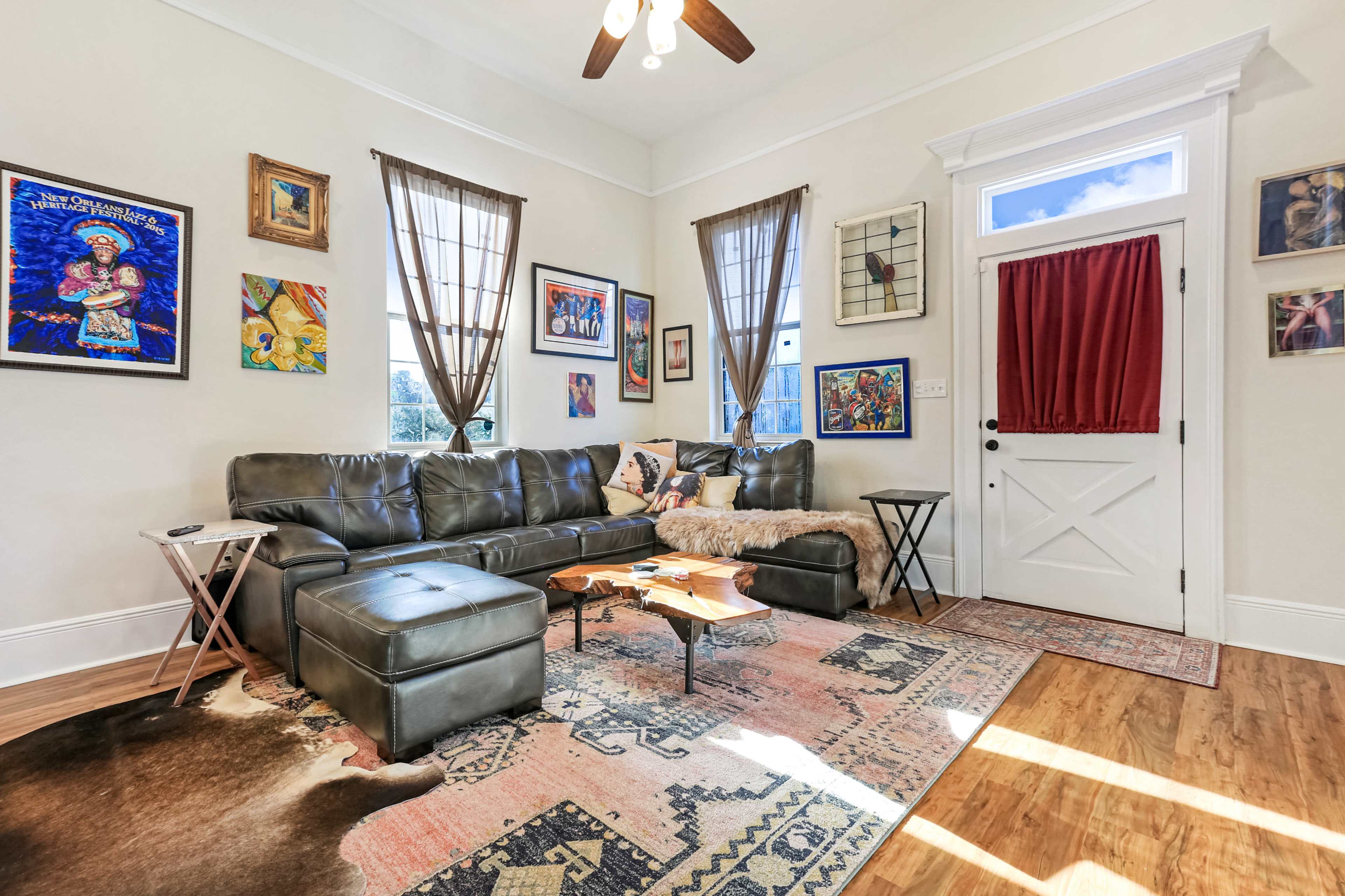 A cozy living room with a leather sectional sofa, various framed artworks on the walls, and a wooden coffee table on a patterned area rug.