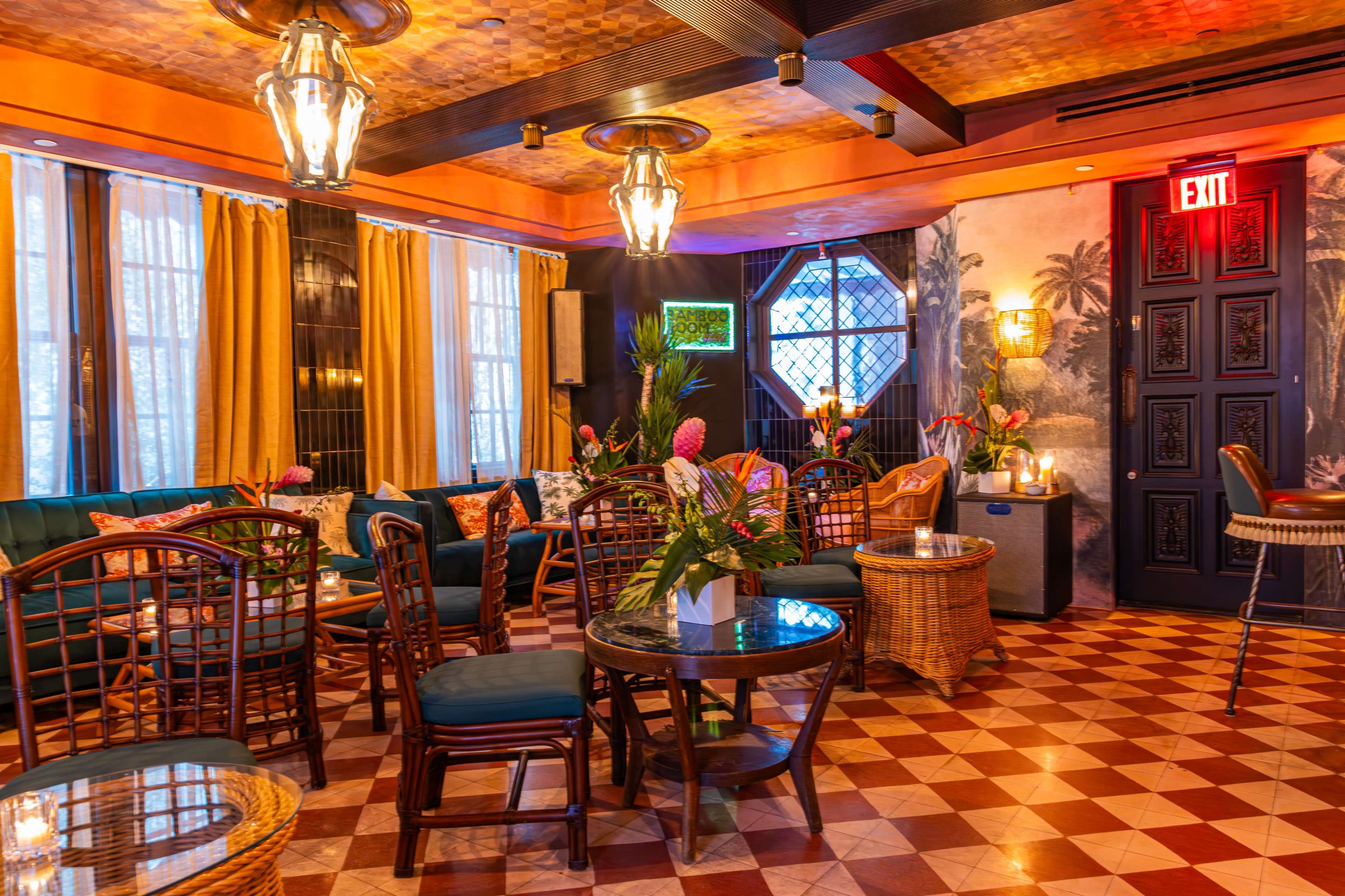 The image shows a stylish lounge area with patterned tiles, wicker seating, and vibrant floral arrangements under warm lighting.