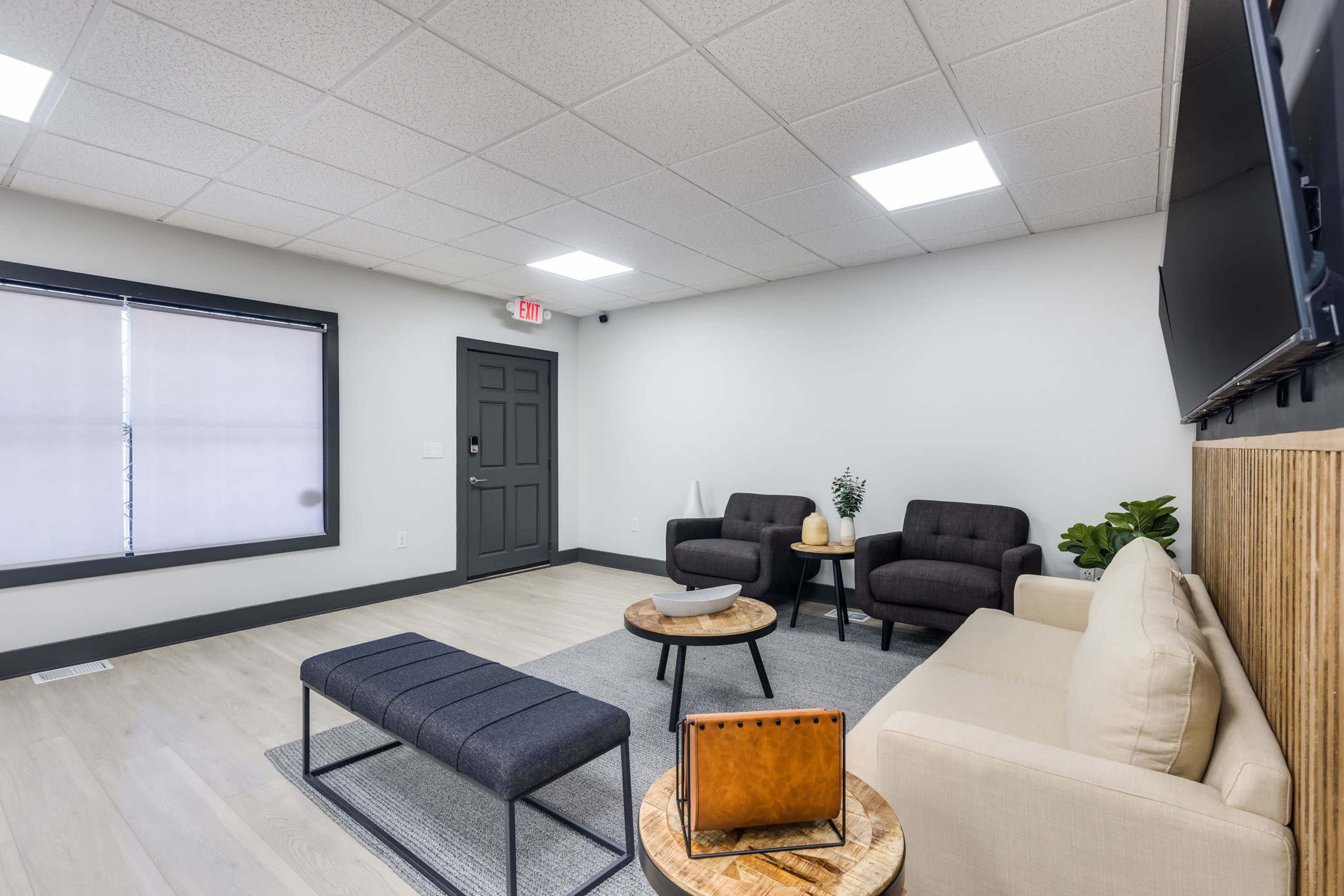 A modern waiting area with a light-colored sofa, two chairs, a coffee table, and a bench, all arranged around a neutral-toned space with overhead lighting.