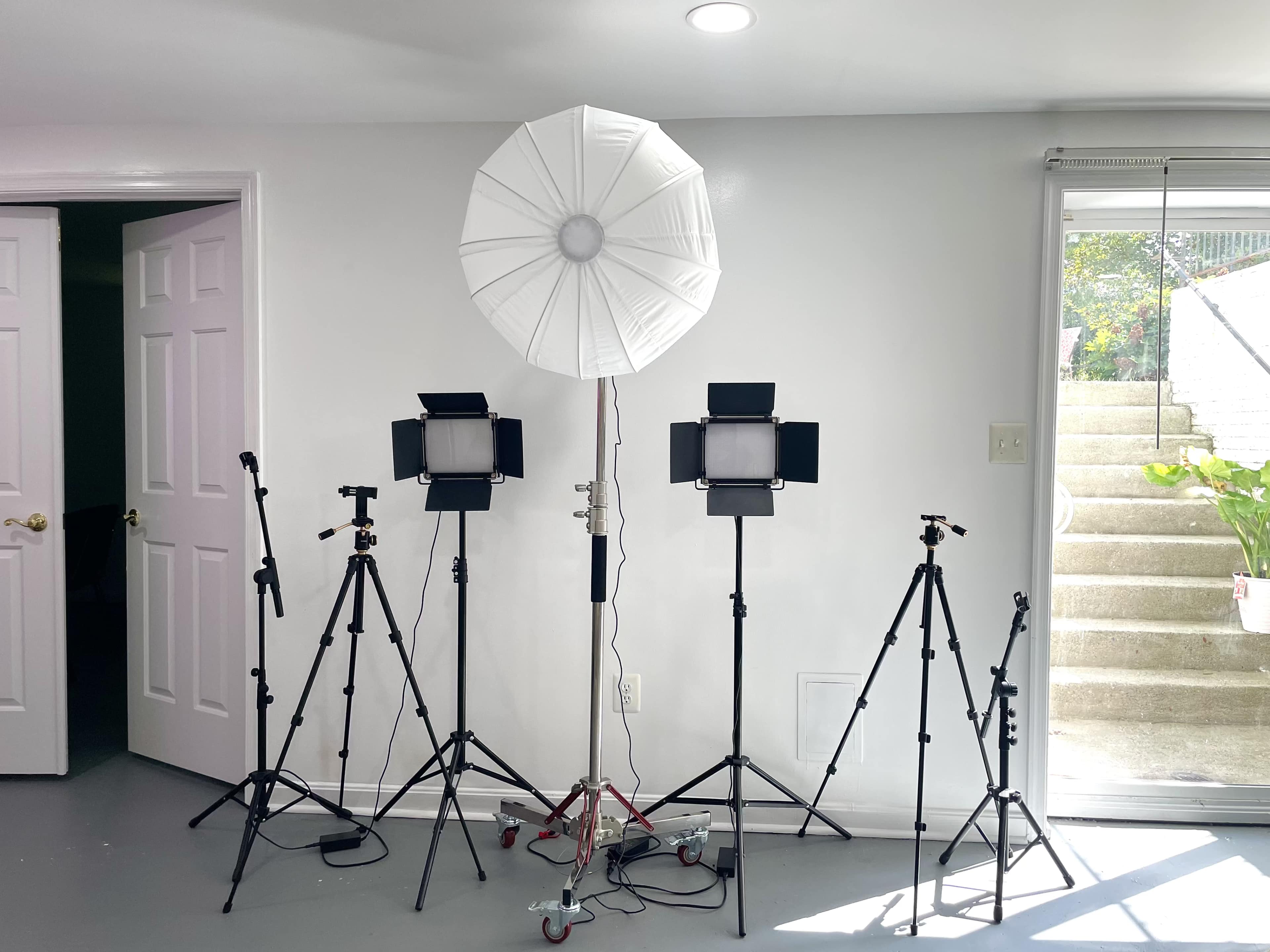 A photography setup featuring a large white umbrella softbox and several tripods with lights arranged in a room near a glass sliding door.