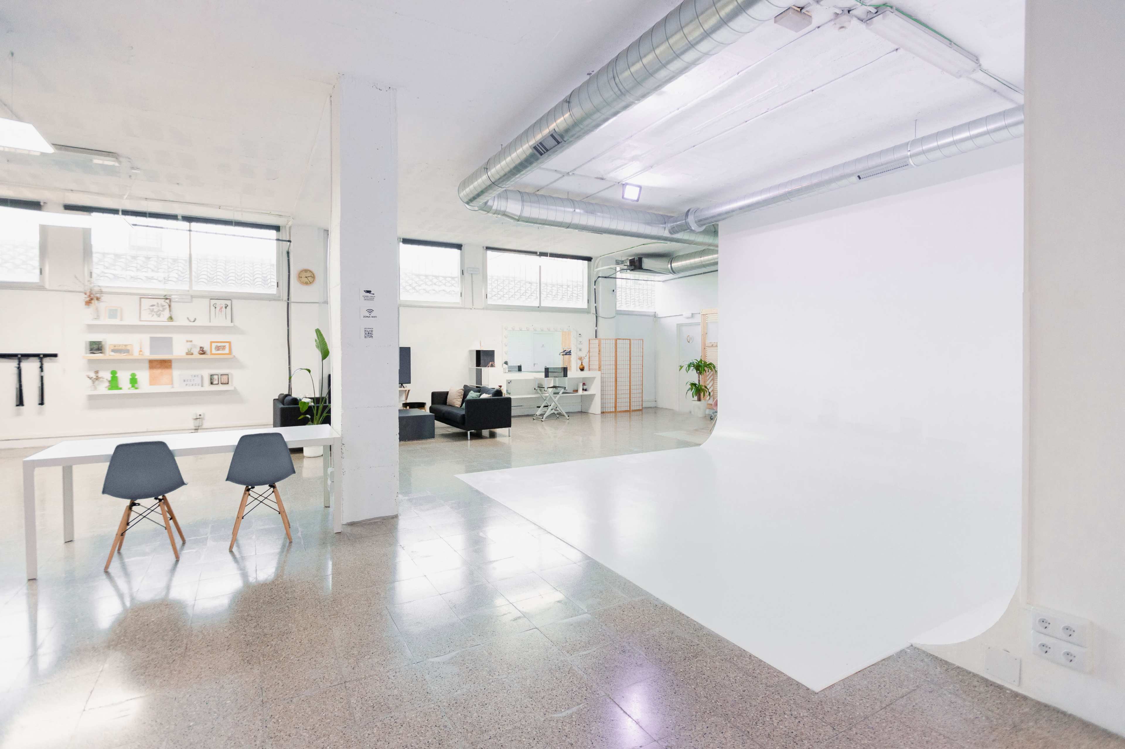 A spacious, modern studio with a white backdrop, a table with chairs, and a seating area.