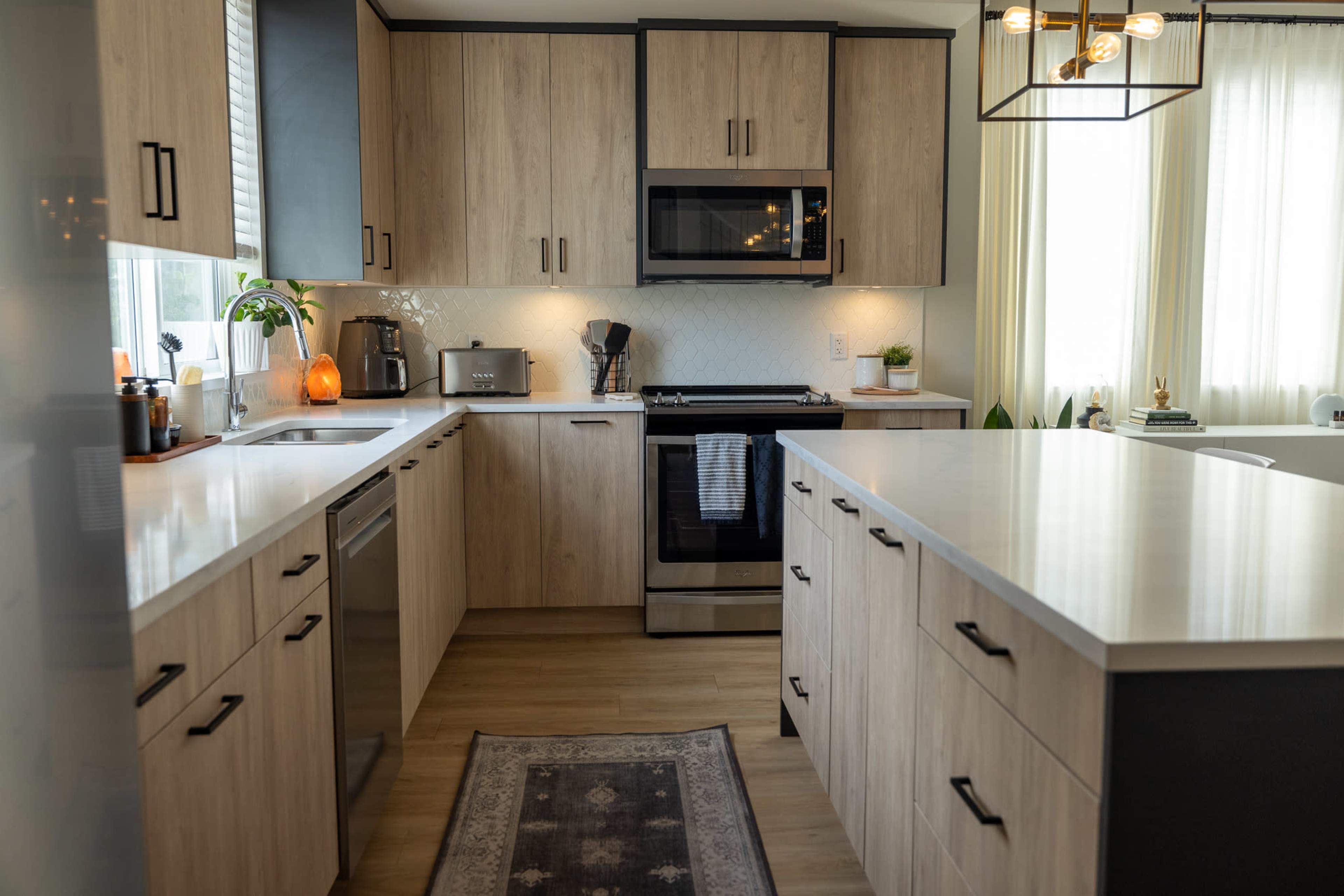A modern kitchen with light wood cabinetry, a stainless steel stove, and a large island countertop.