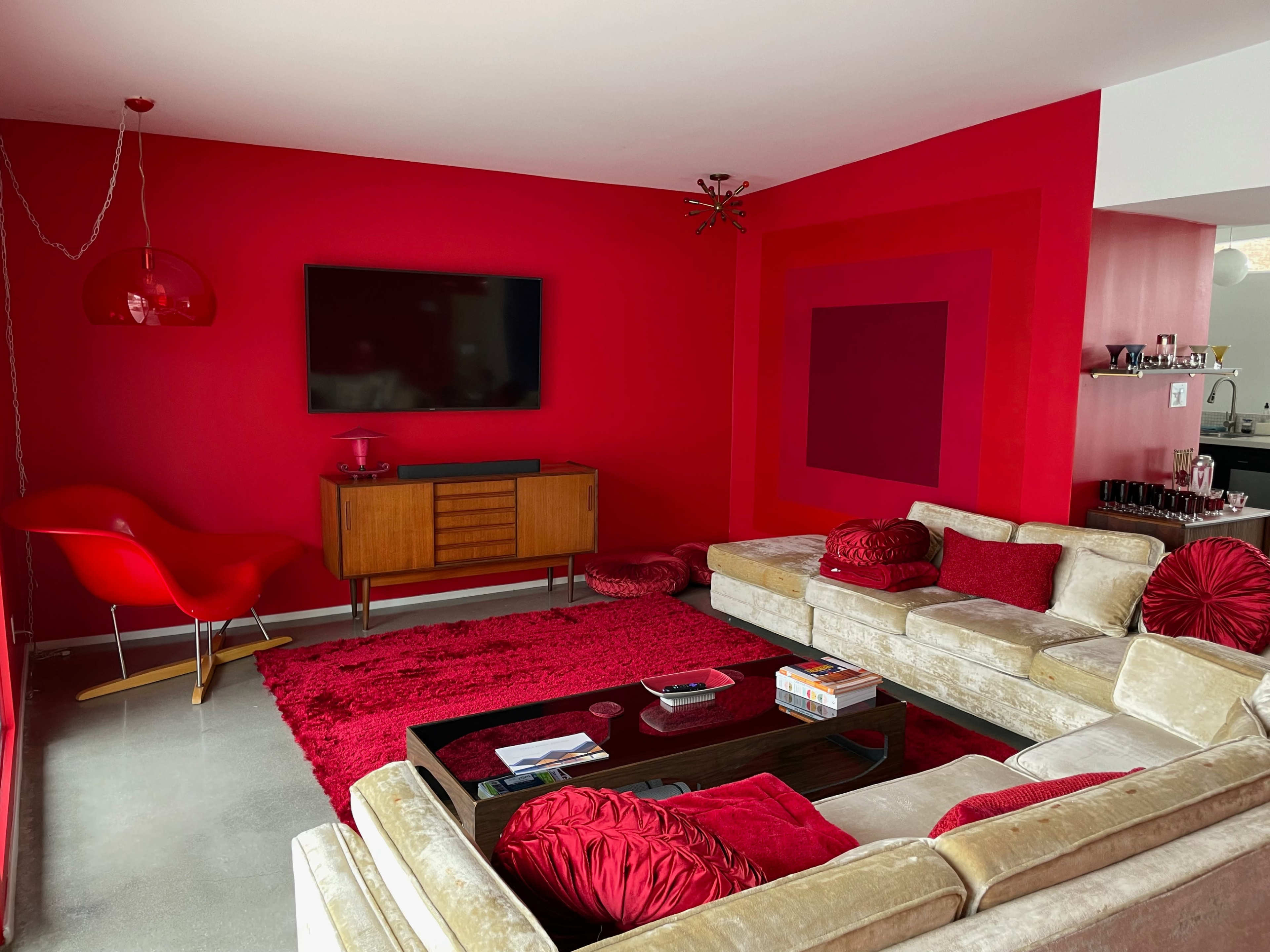 The living room features a red accent wall, a beige sectional sofa, and a modern coffee table on a red rug.