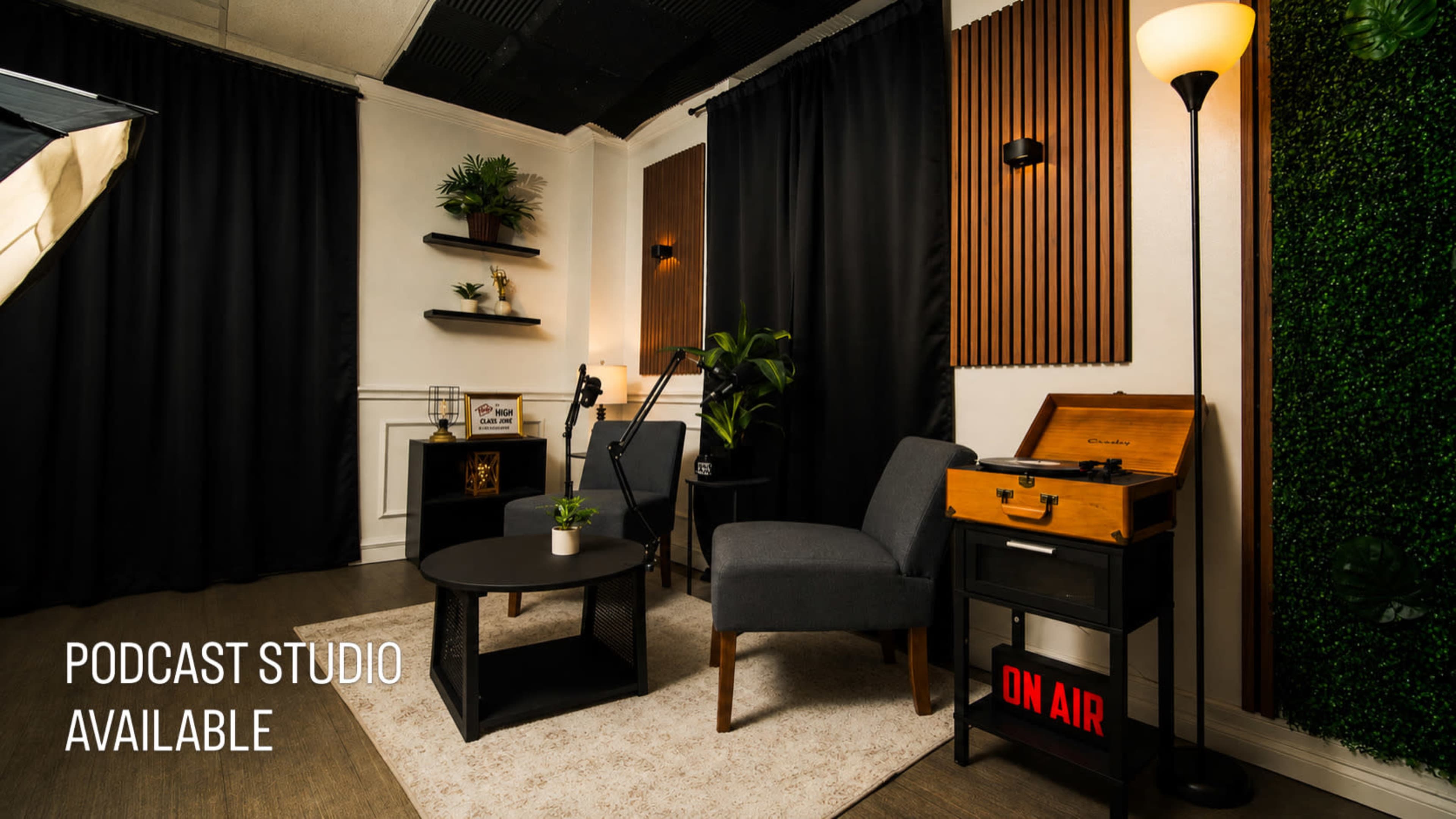 The image shows a cozy podcast studio featuring two chairs, a small table, decorative plants, and a sign indicating that the studio is available for use.