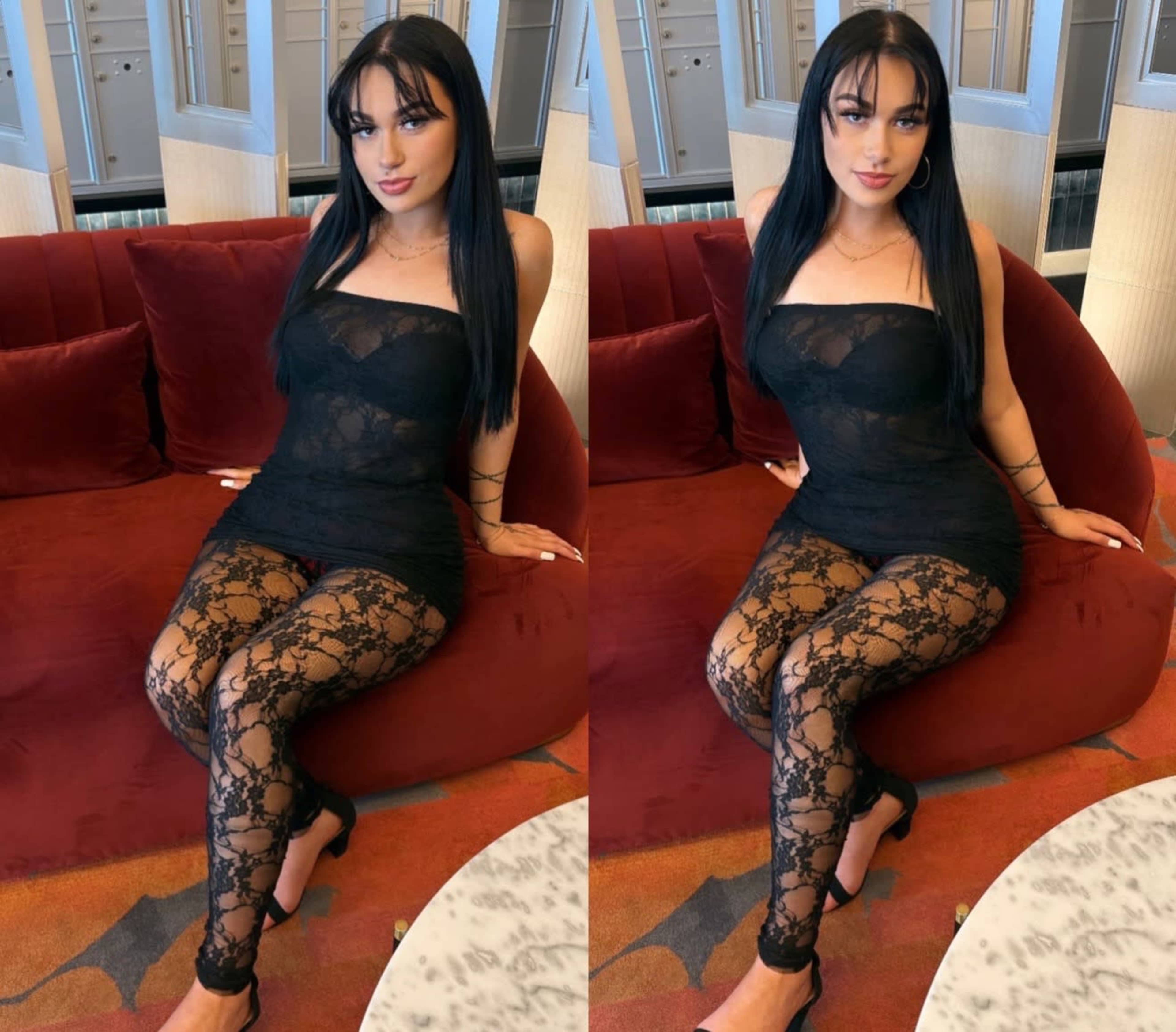 A person wearing a black lace outfit sits on a red velvet couch in an indoor setting.