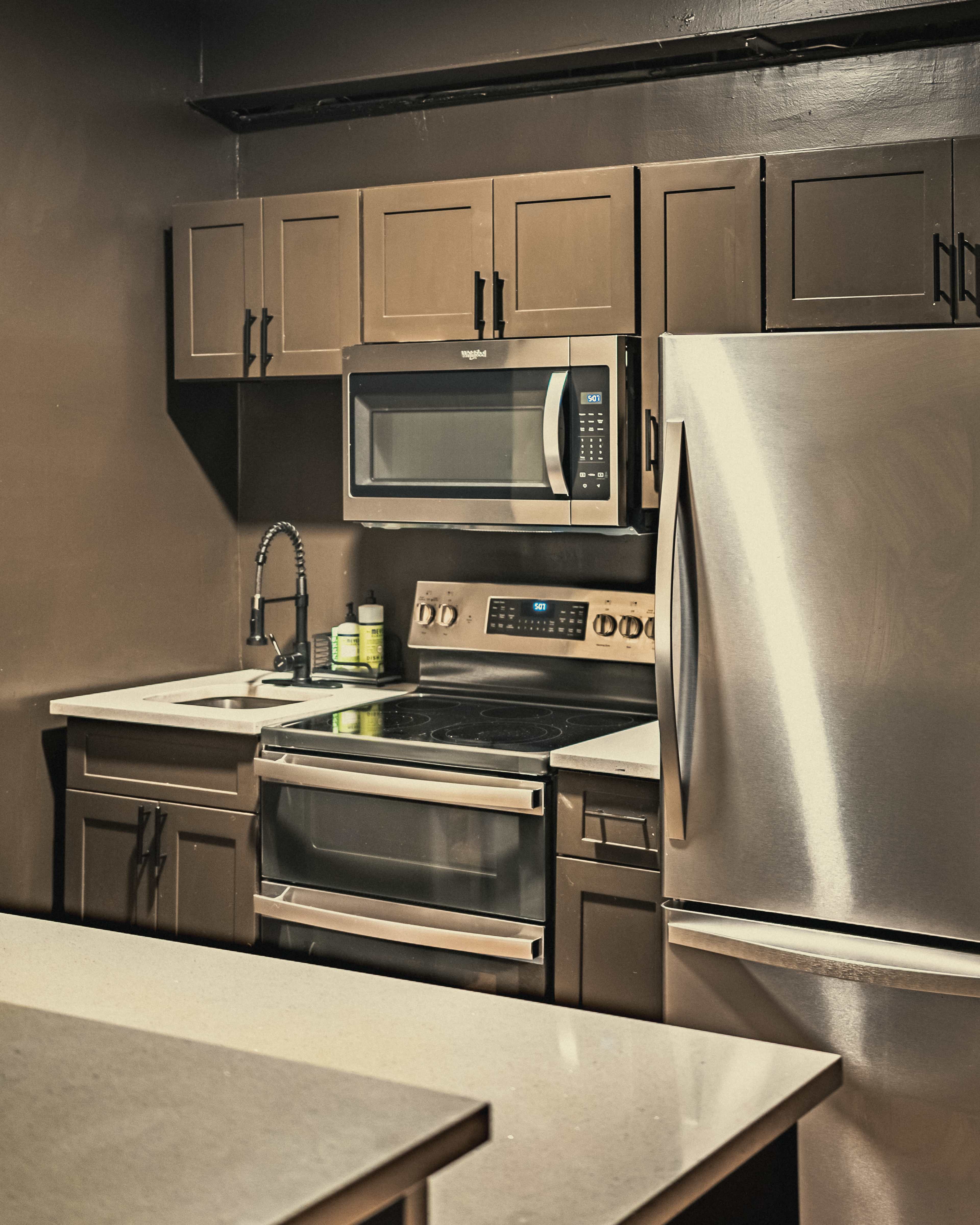 The image shows a kitchen with dark cabinets, a stainless steel refrigerator, an oven, and a microwave above the stove.