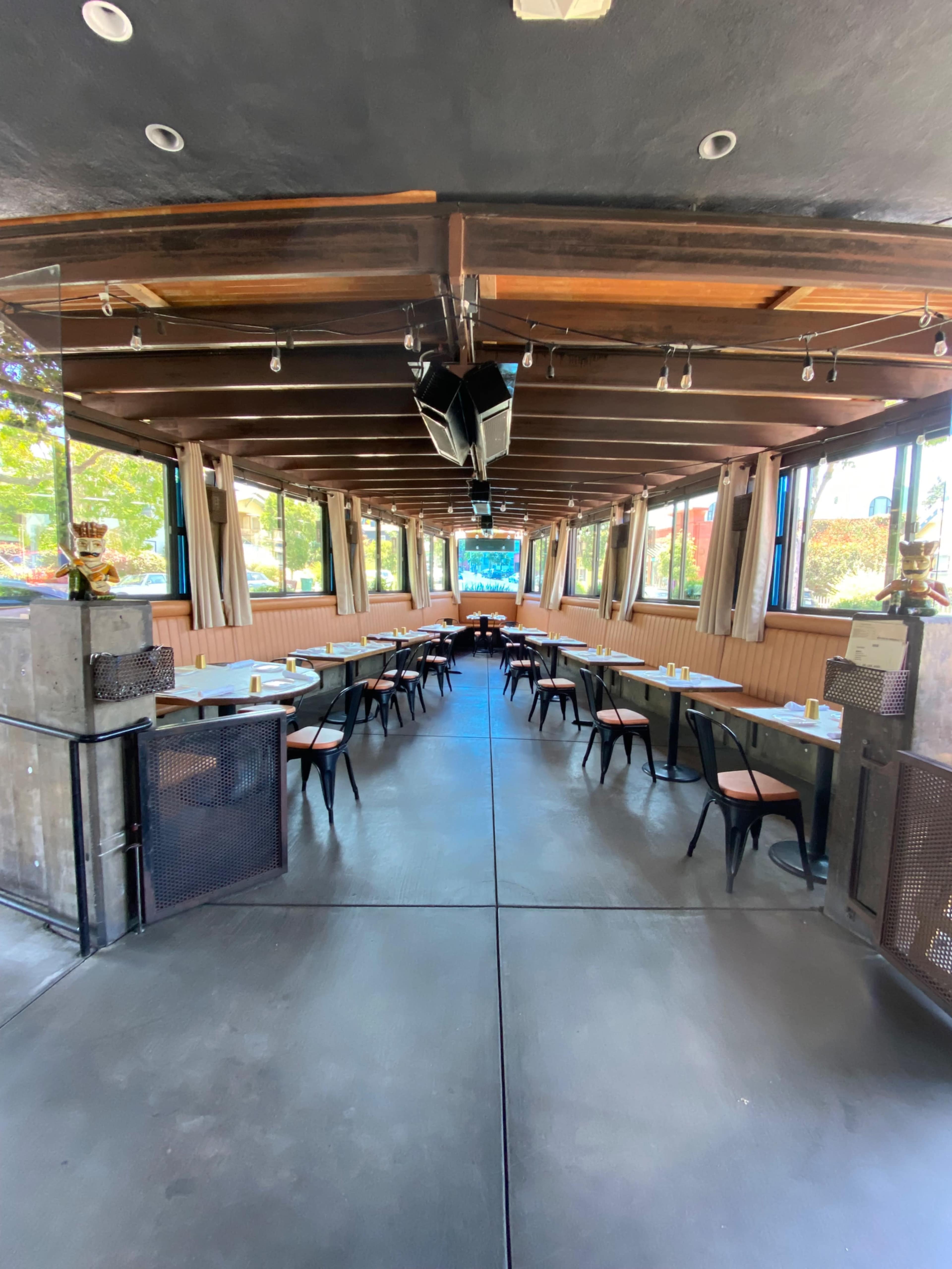 A spacious restaurant interior with long tables arranged parallel to the walls and large windows providing natural light.