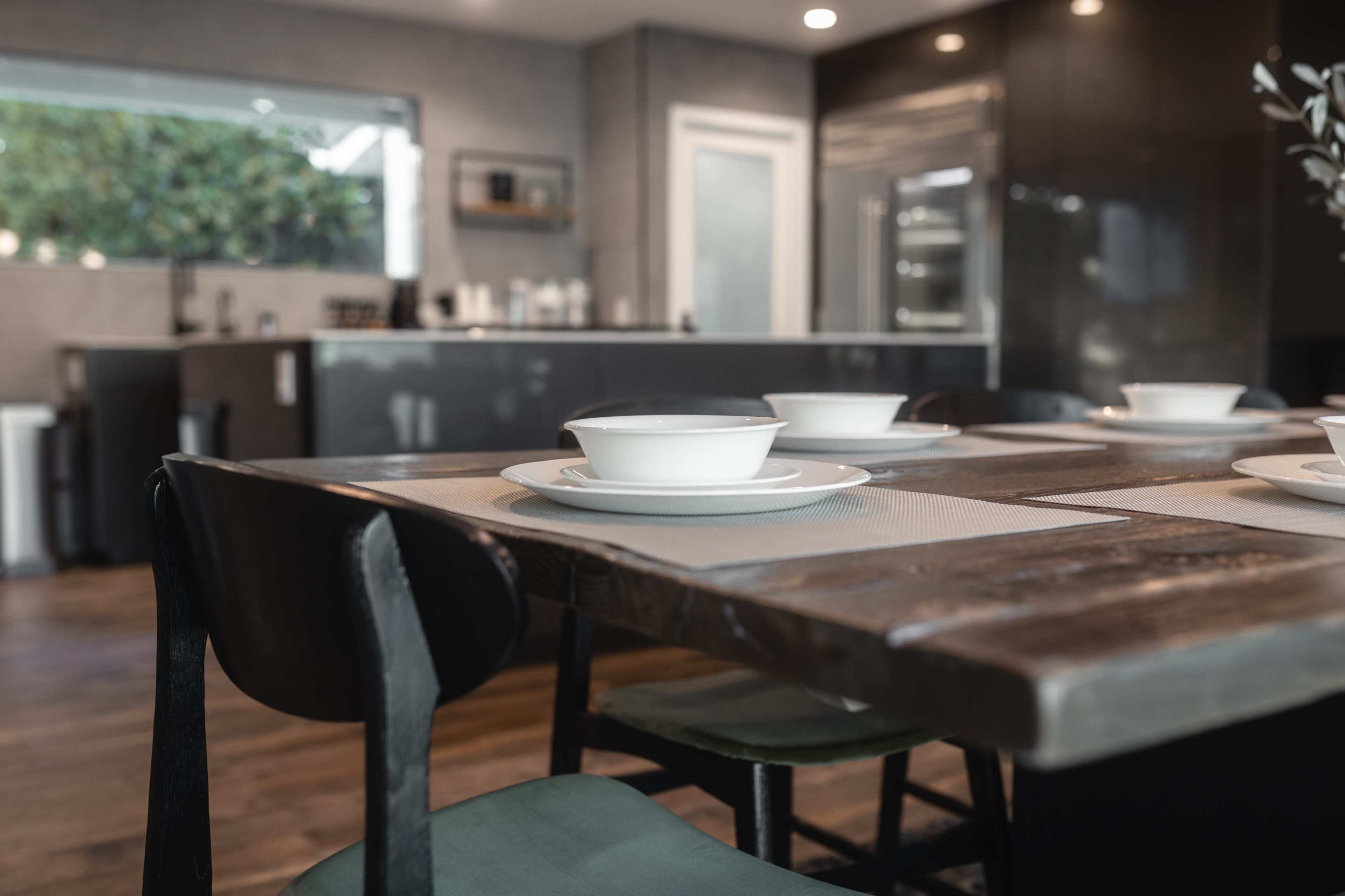 A wooden dining table is set with white bowls, while a modern kitchen is visible in the background.