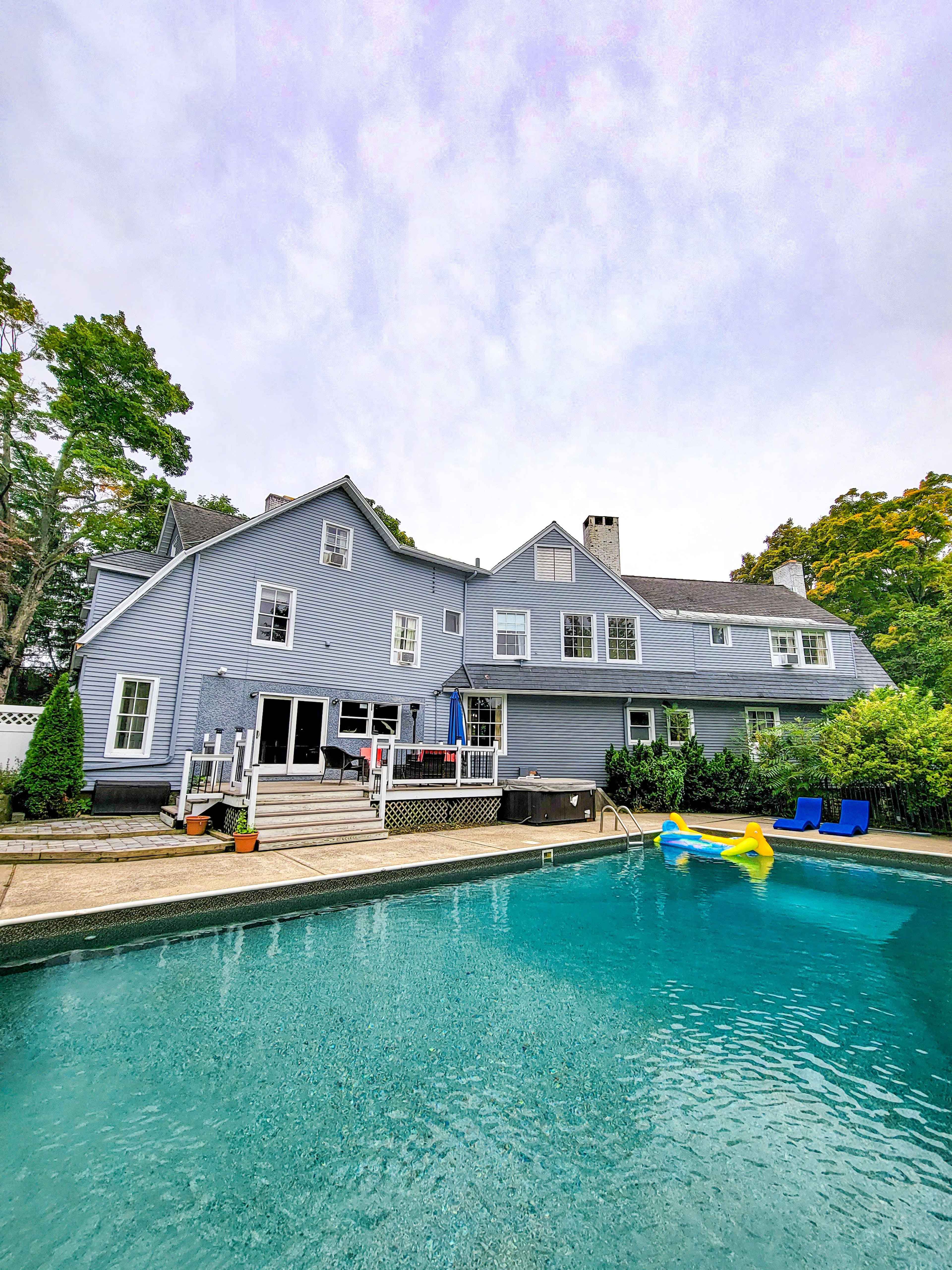A two-story gray house with a swimming pool and a patio area is surrounded by trees.