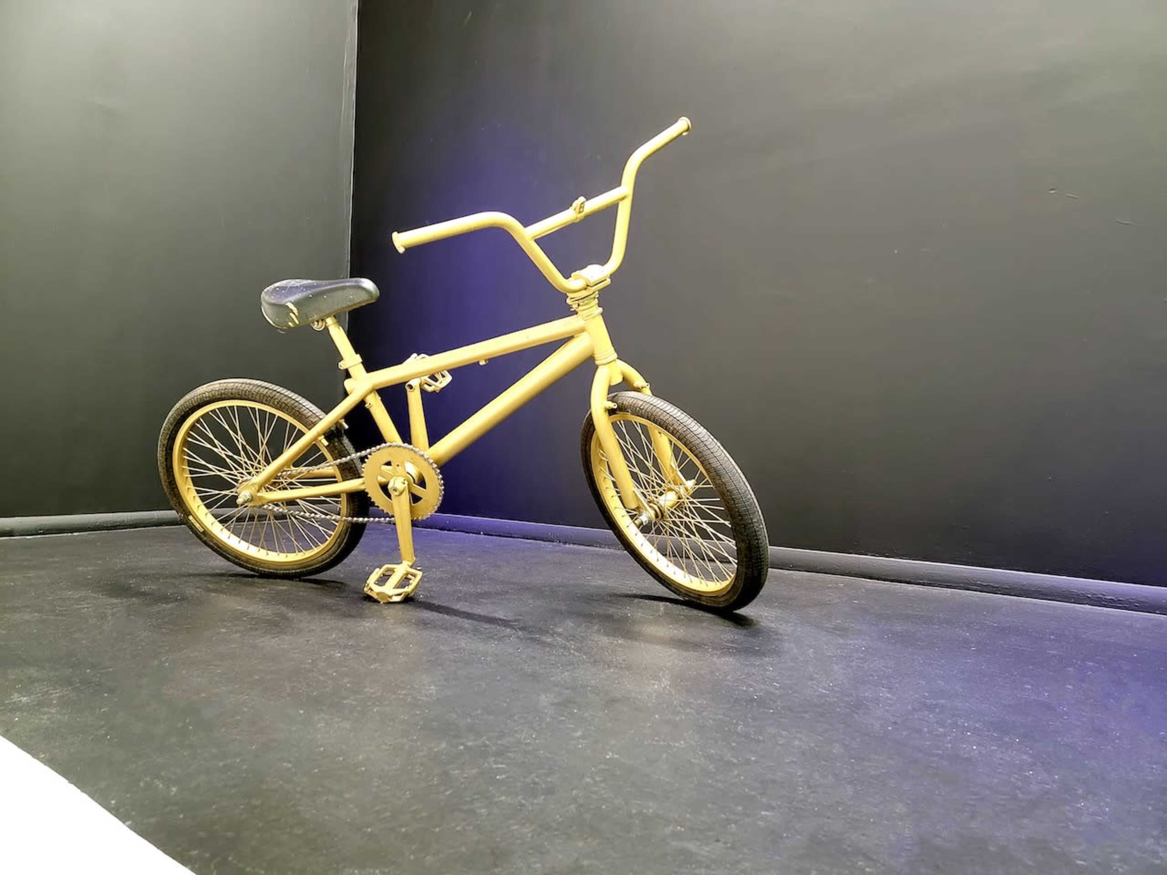 A yellow bicycle with a low frame and wide handlebars is placed against a black background.