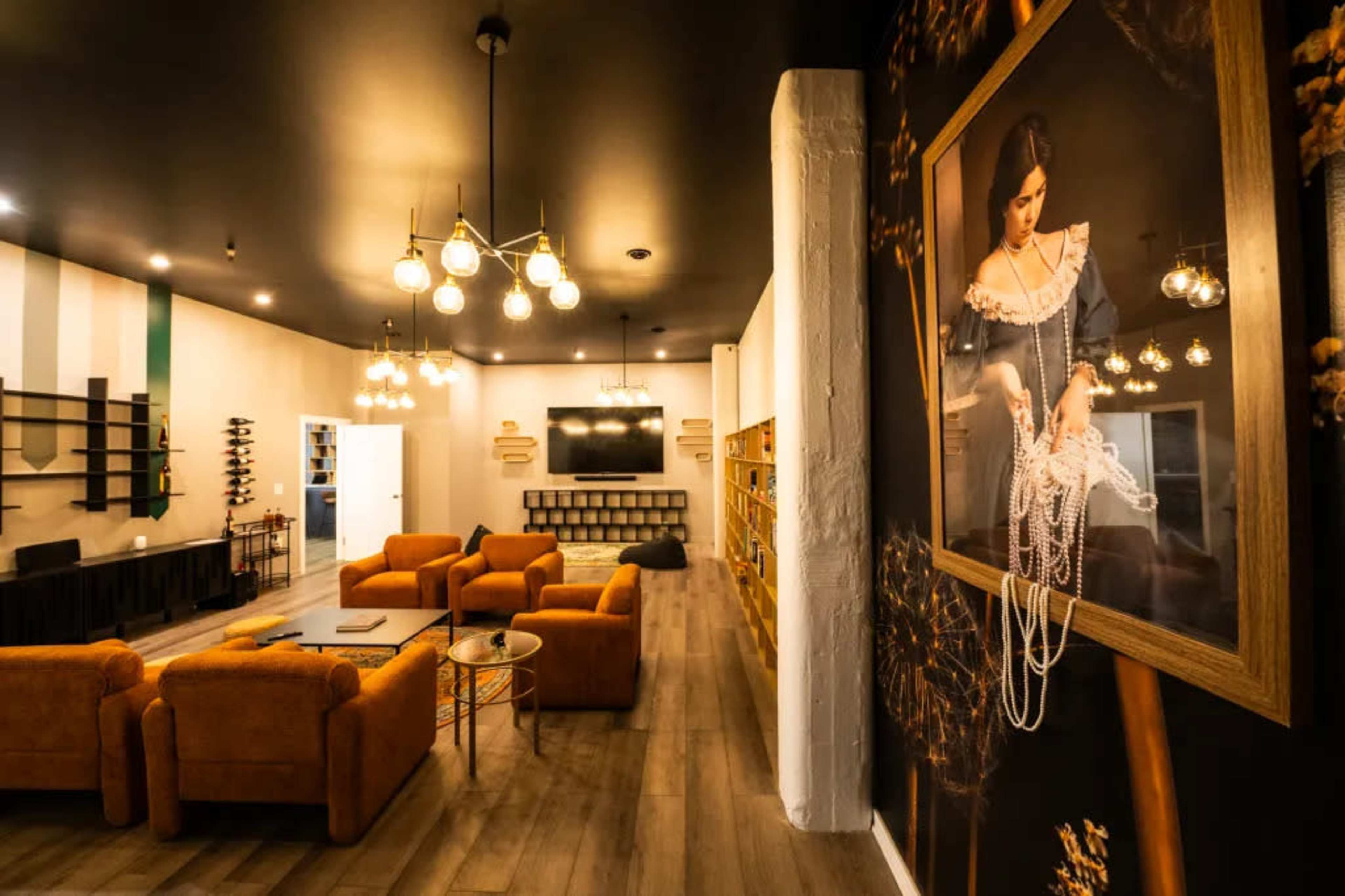 A modern lounge area with orange sofas, decorative lighting, and a large wall mural of a woman wearing pearls.