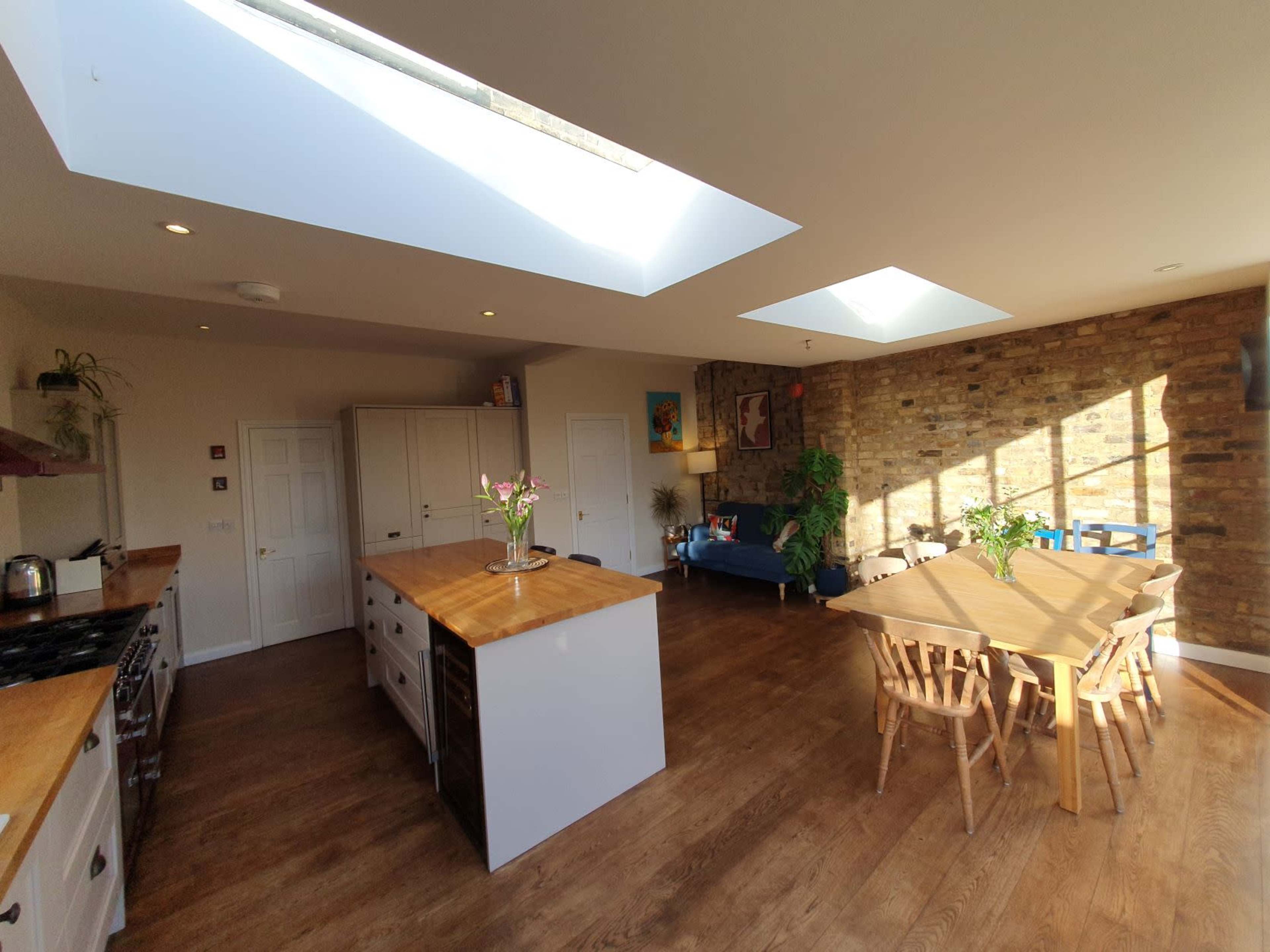 The open kitchen features an island with a wooden countertop, a dining table, and large windows that allow natural light to illuminate the space.