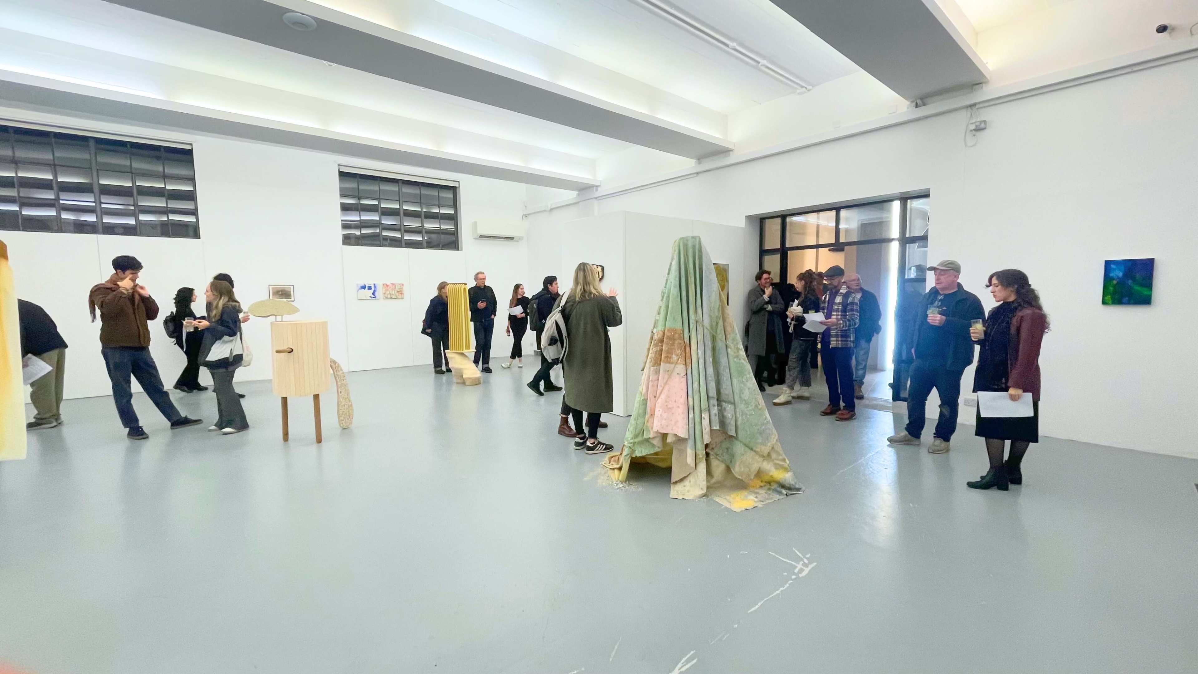 A group of people interacts in an art gallery featuring various artworks displayed on the walls and sculptures in the center of the room.