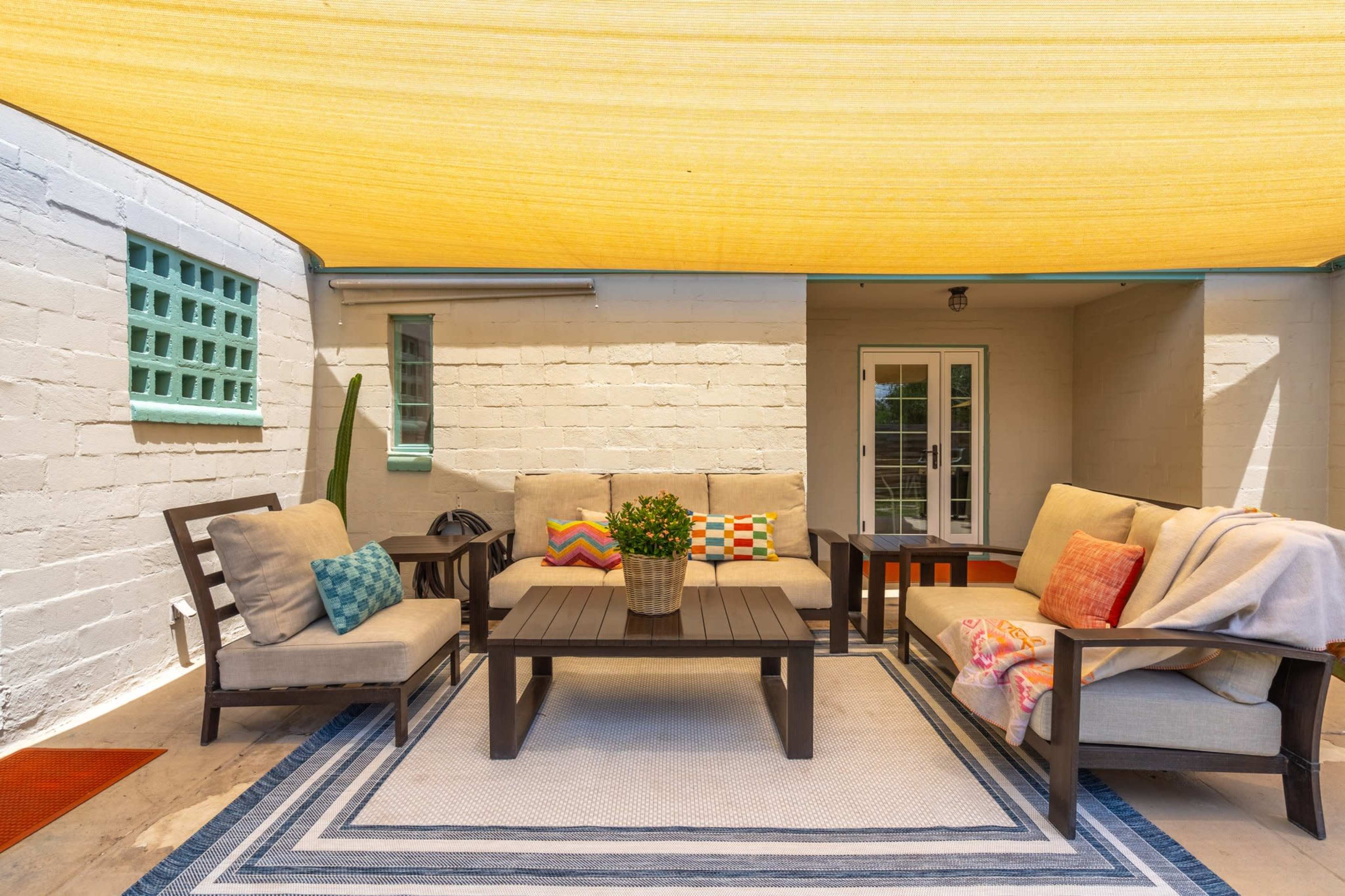 The image shows a shaded outdoor seating area with a table, chairs, and decorative pillows on a patio.