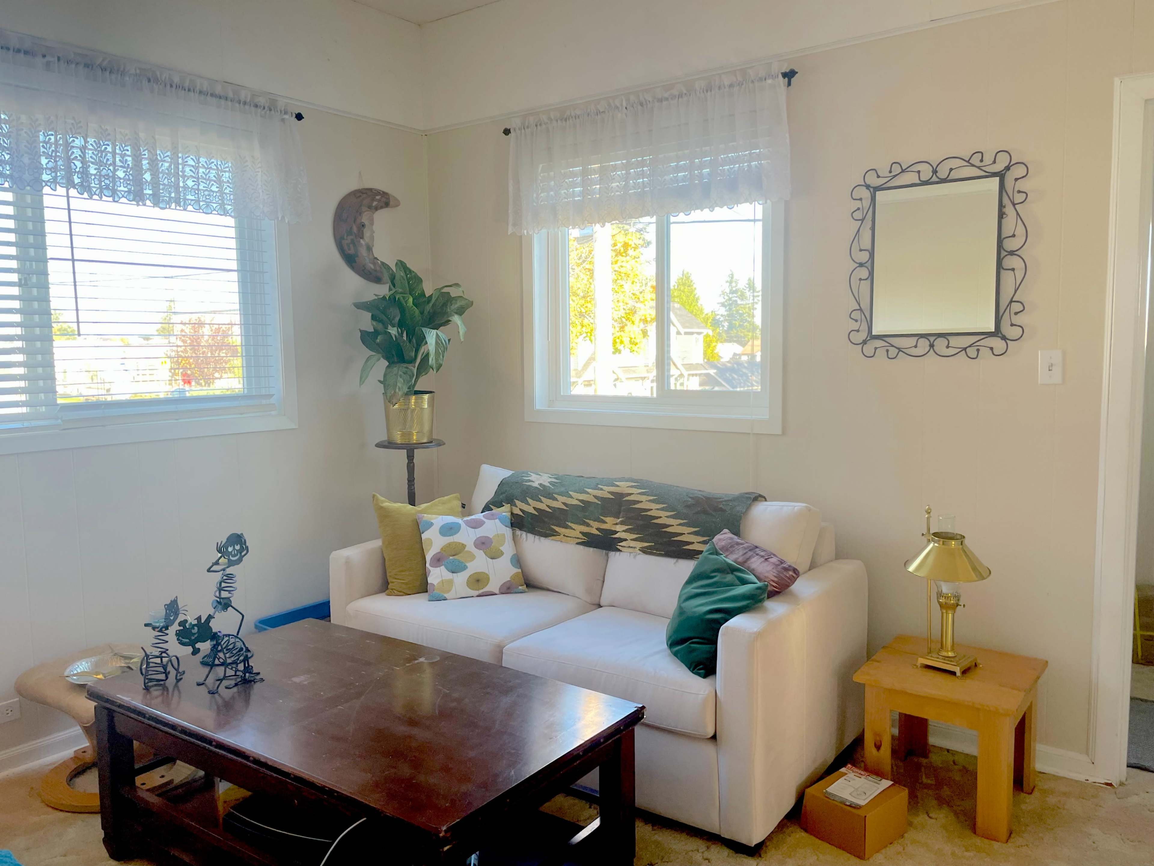 A cozy living room with a white sofa, a wooden coffee table, and large windows allowing natural light to enter.