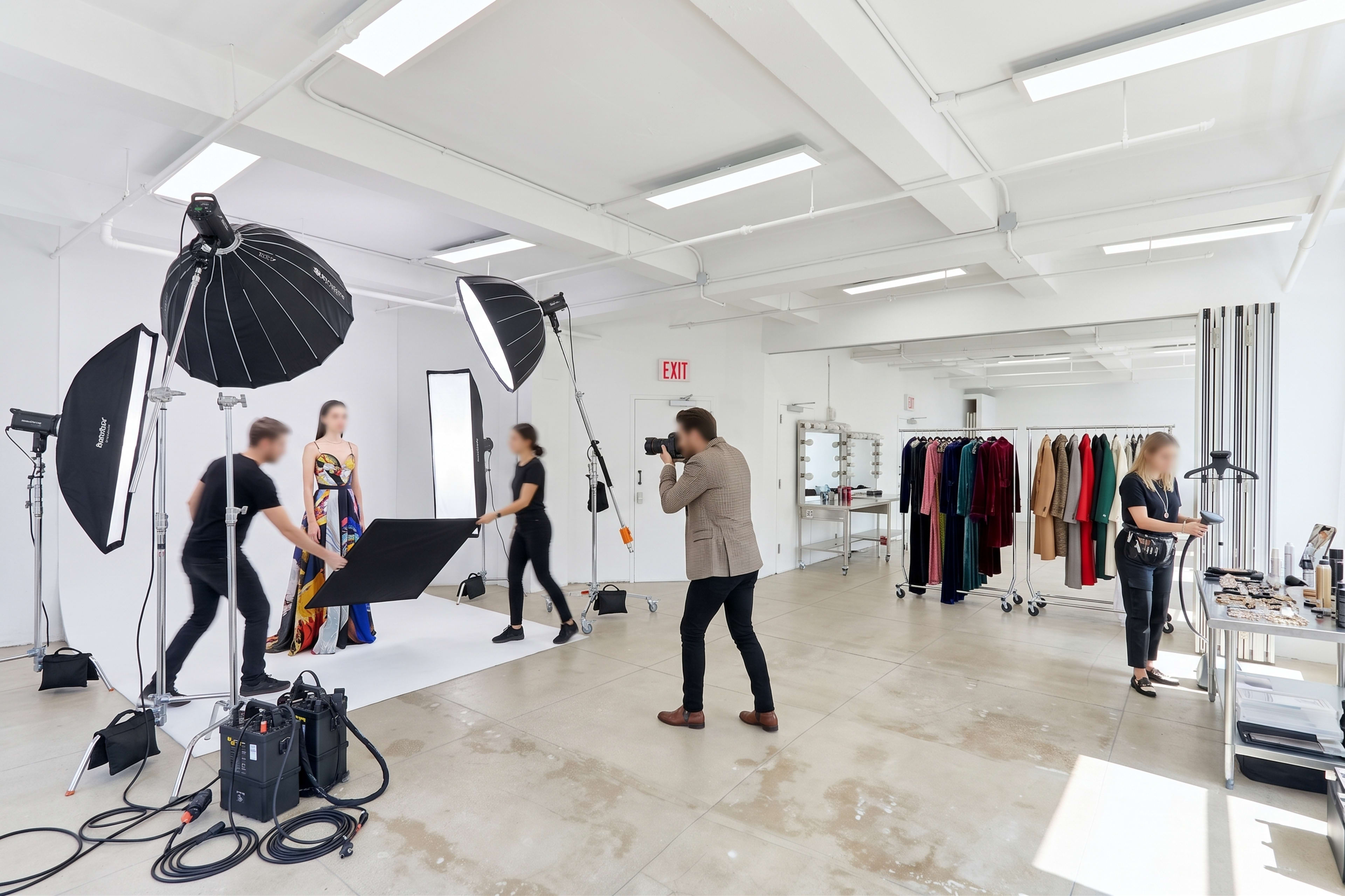A fashion photoshoot is taking place in a well-lit studio, featuring a model in a colorful dress surrounded by photographers and assistants.