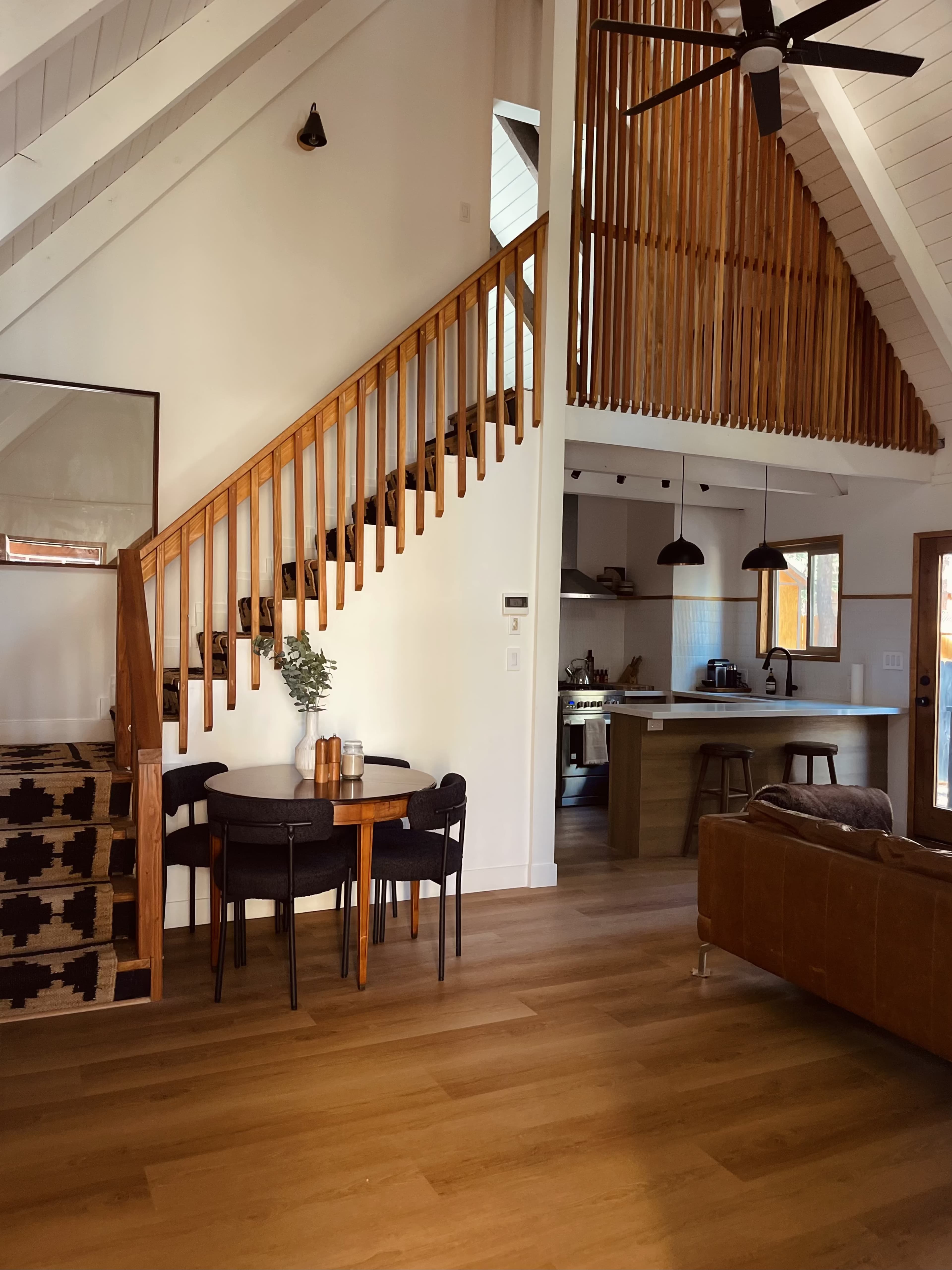 The image shows a modern interior of a home featuring a wooden staircase, a dining area with a round table, and a kitchen visibly integrated into the open living space.