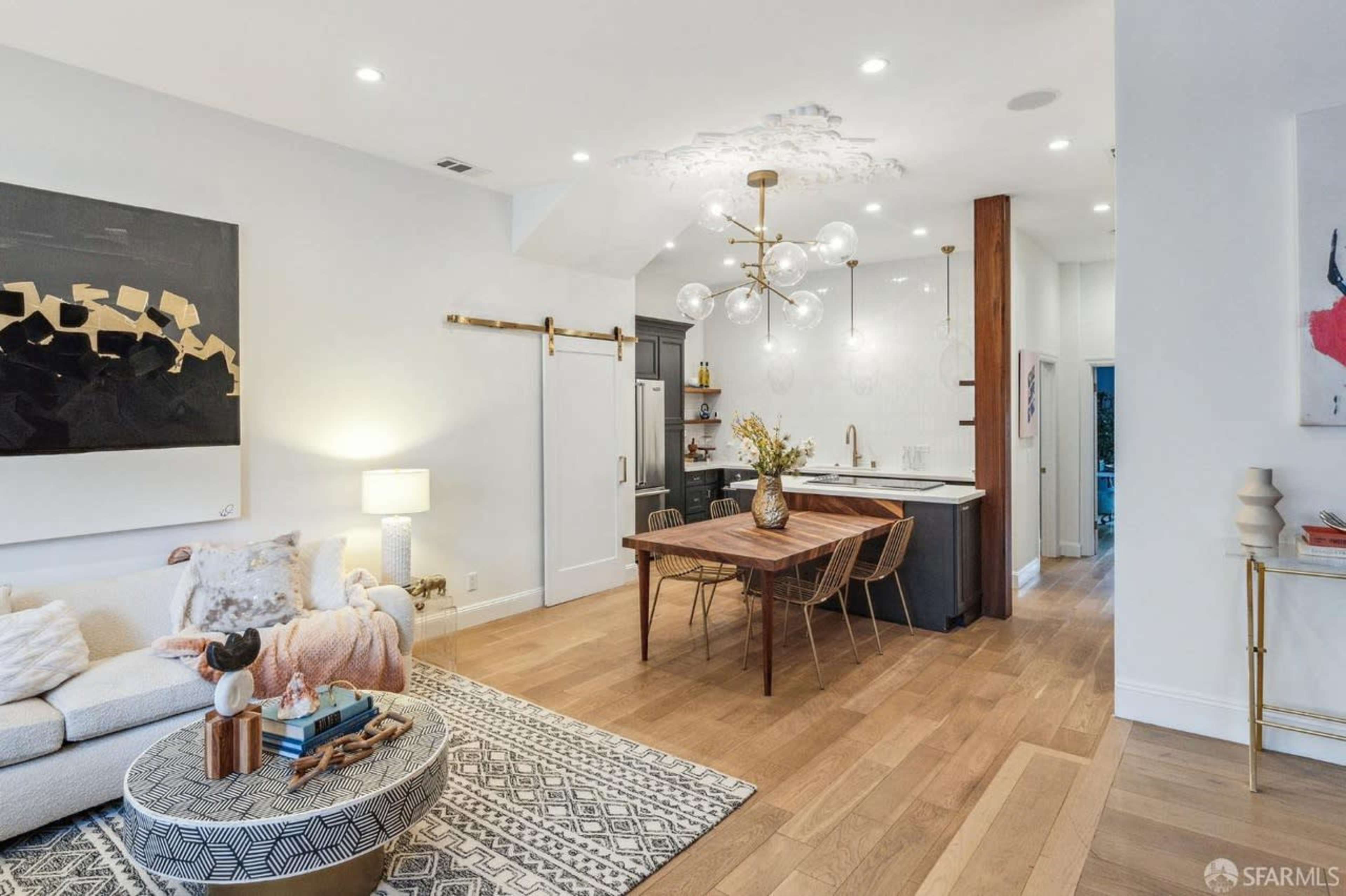 A modern living space featuring a sofa, a round coffee table, a dining table with chairs, and a kitchen area with a large pendant light.