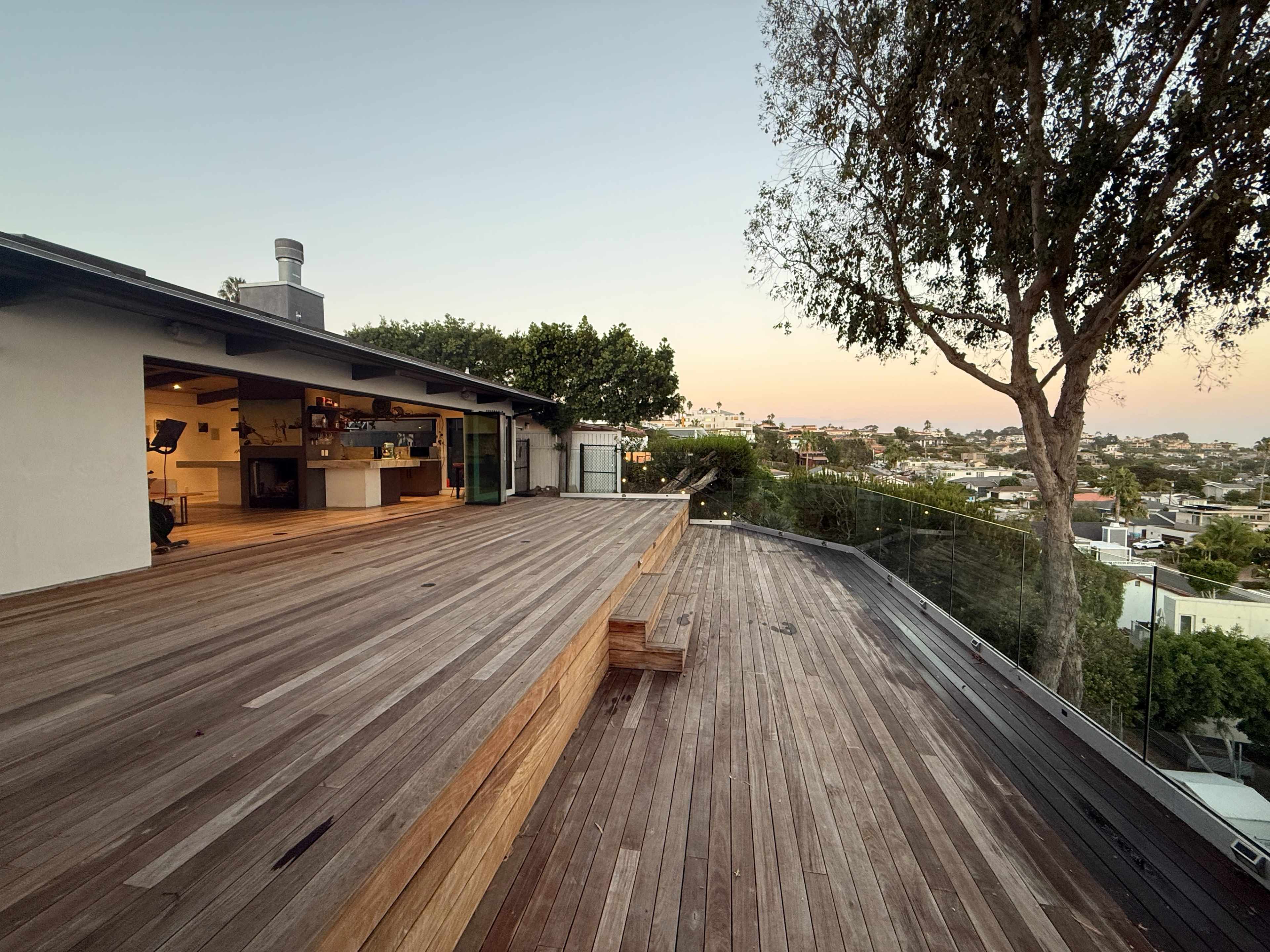 A spacious wooden deck extends from a modern home, overlooking a neighborhood with trees and distant hills.