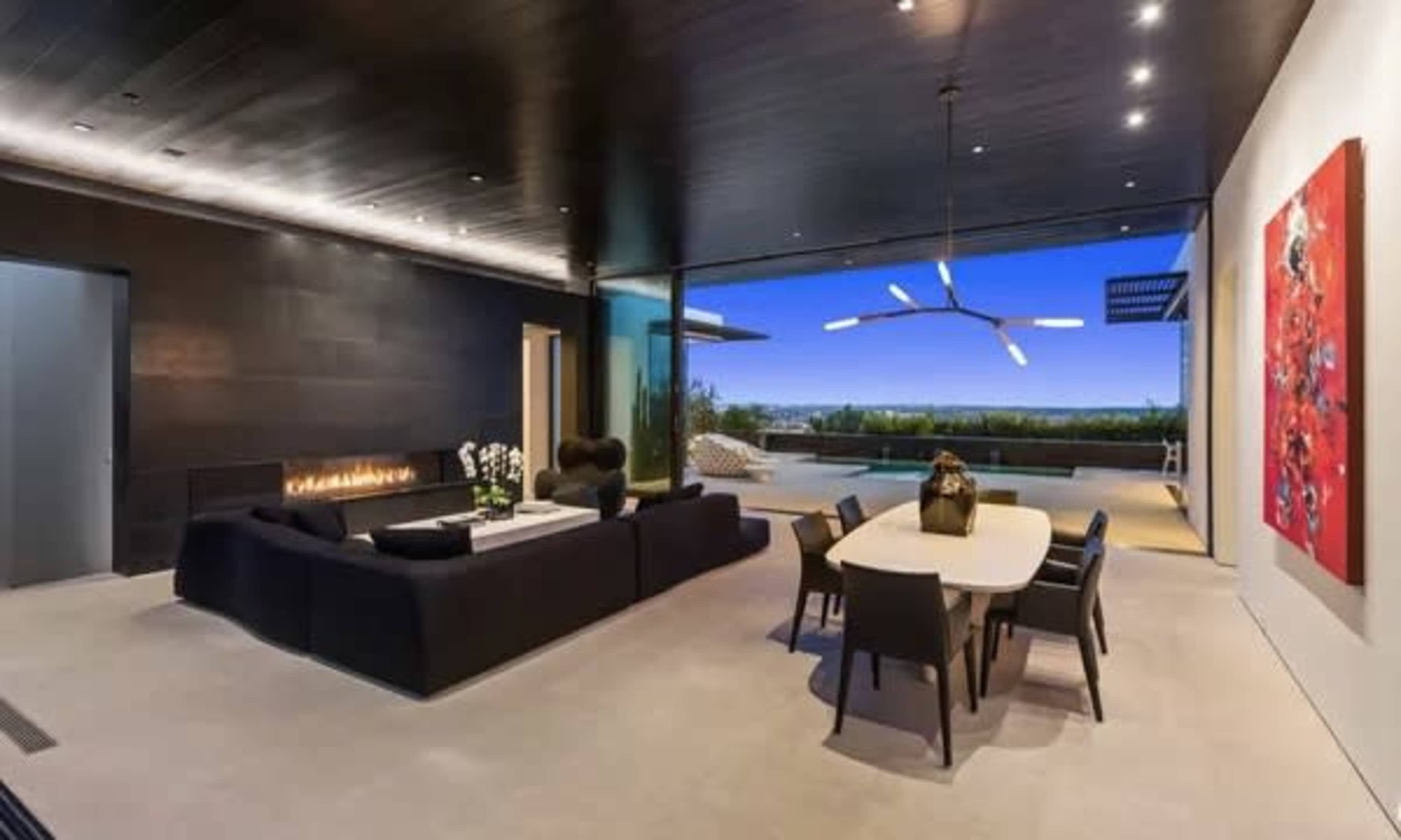 The image shows a contemporary open-concept living space with a sleek black sectional sofa, a dining table, and large glass doors that open to a scenic outdoor view.