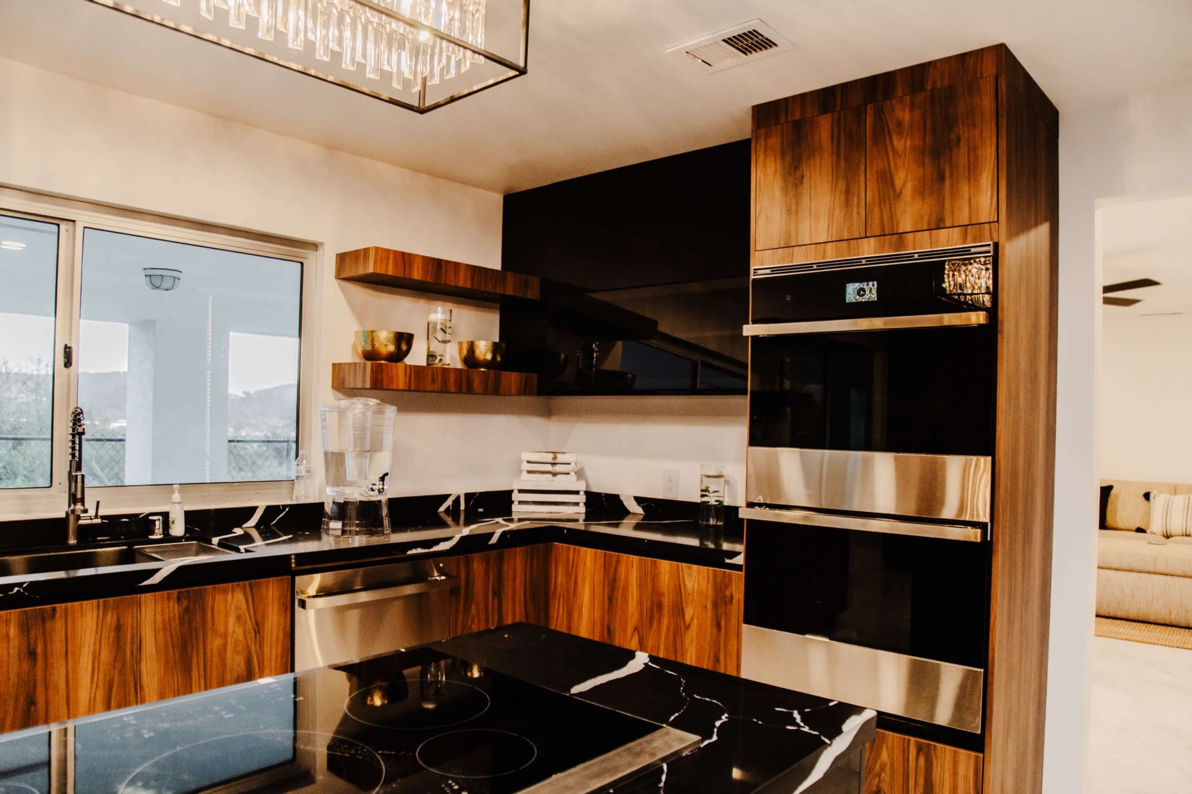 A modern kitchen featuring dark wood cabinetry, a marble countertop, stainless steel appliances, and open shelves with decorative items.