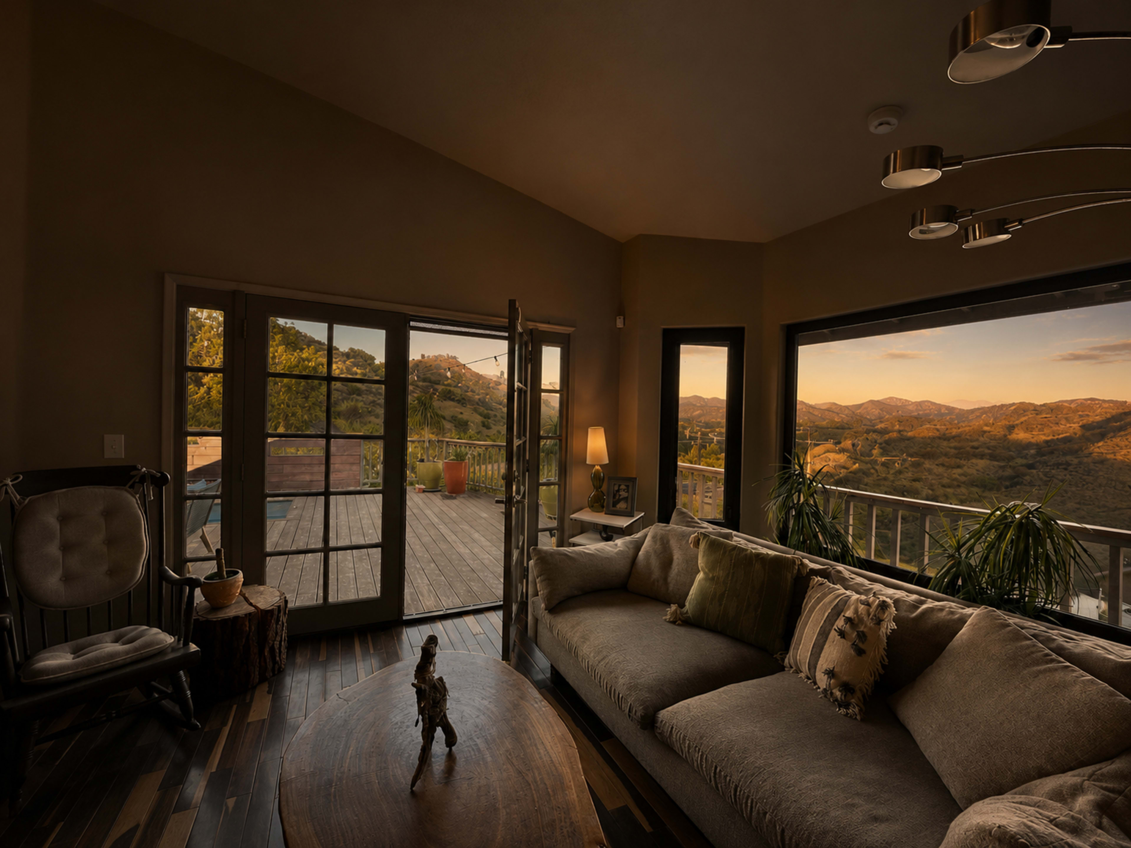 A cozy living room features large windows with scenic views of rolling hills at sunset and a wooden deck.