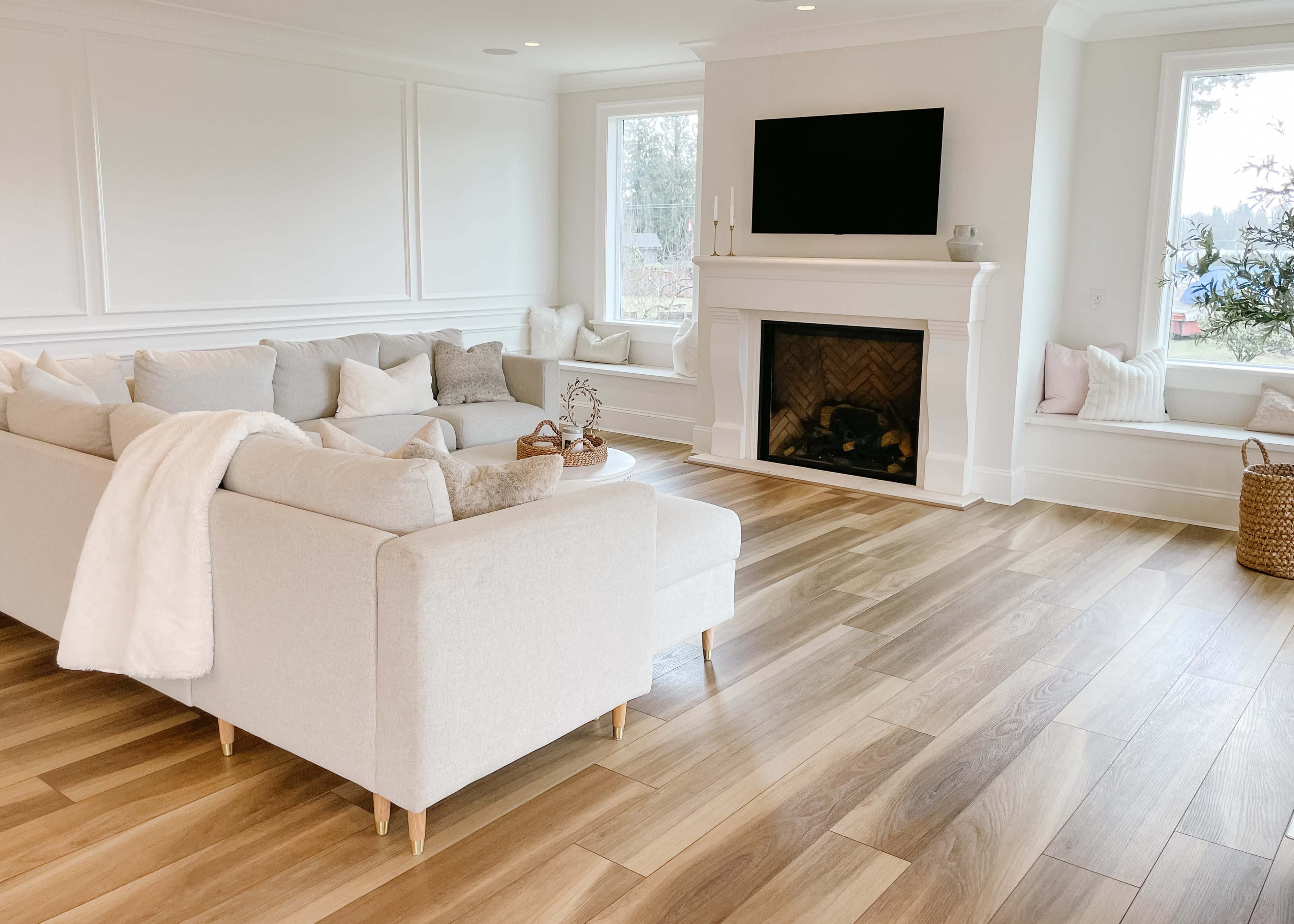 A bright, modern living room with a light-colored sectional sofa, a fireplace, and large windows.