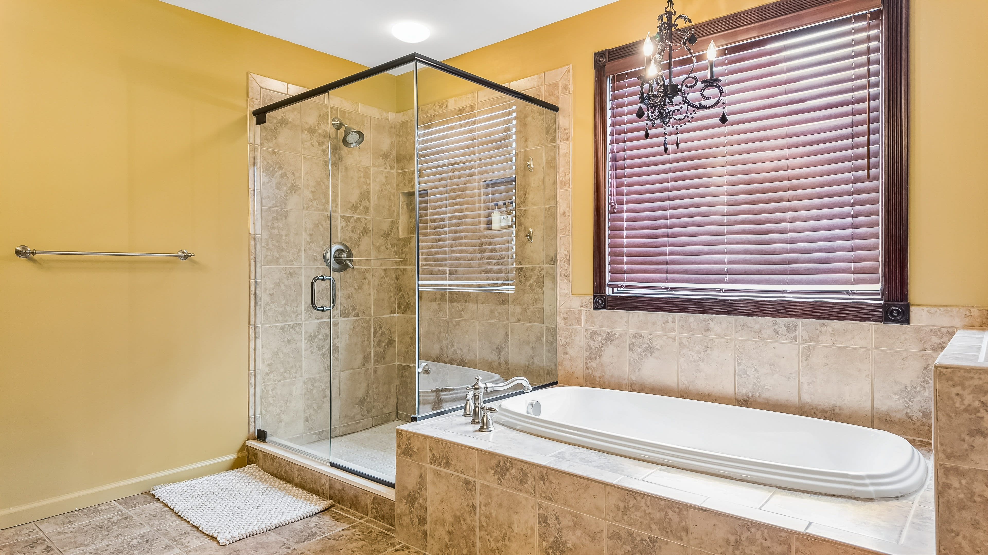 The image shows a bathroom featuring a glass shower enclosure and a white bathtub surrounded by beige tiled walls.