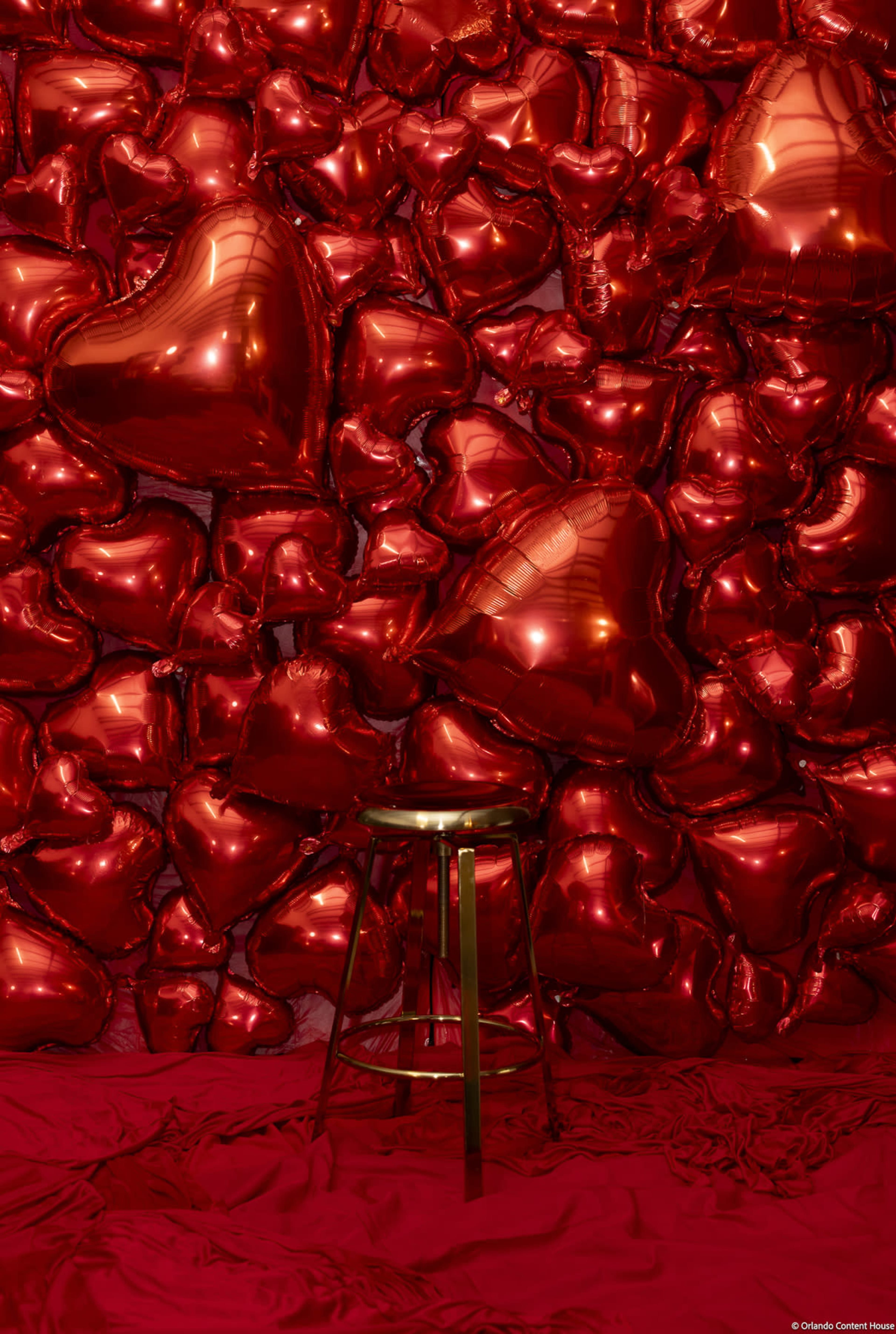 A gold stool is positioned in front of a wall covered in red heart-shaped balloons.